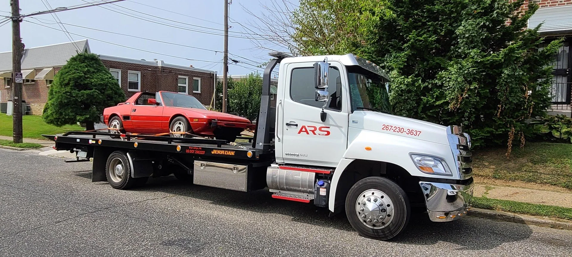 White tow truck carrying a red sports car on a city street.