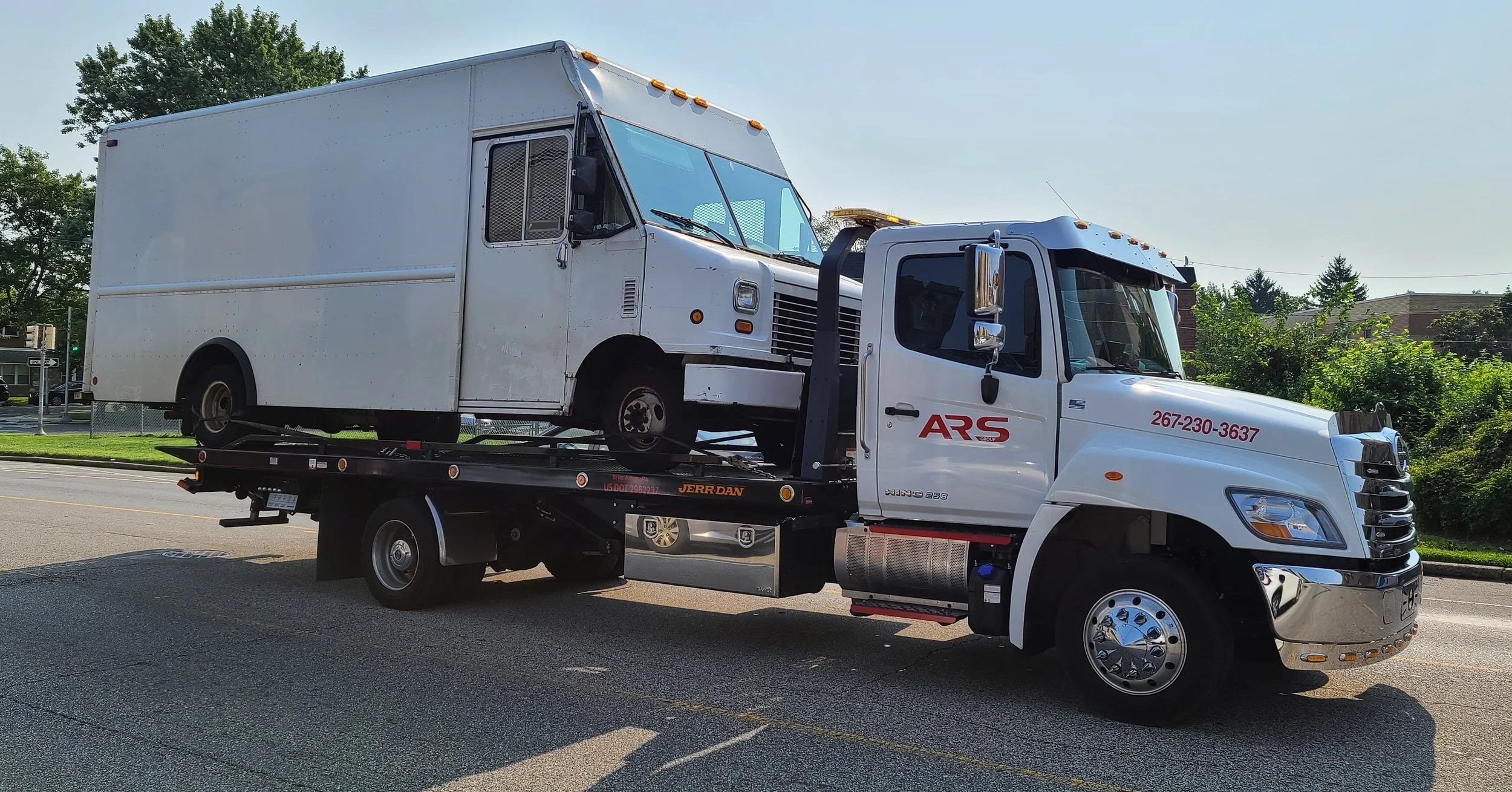 White flatbed tow truck carrying an old, white panel delivery truck