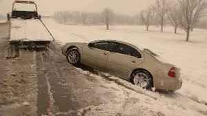 A car stuck in snow beside a snowplow on a snowy road during winter.