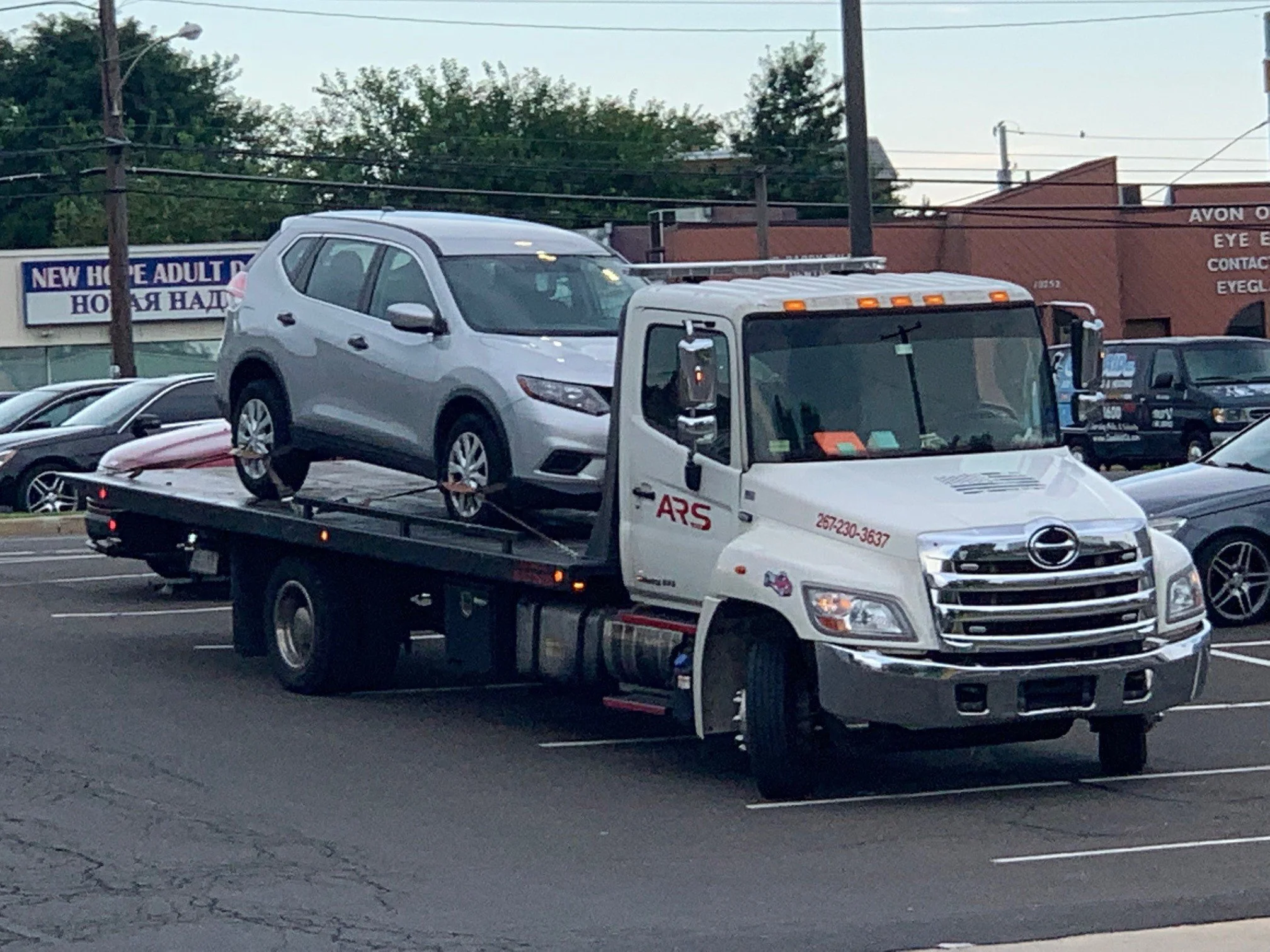 Tow truck carrying a silver car in a parking lot