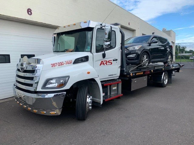 White tow truck carrying a black SUV at a loading dock area