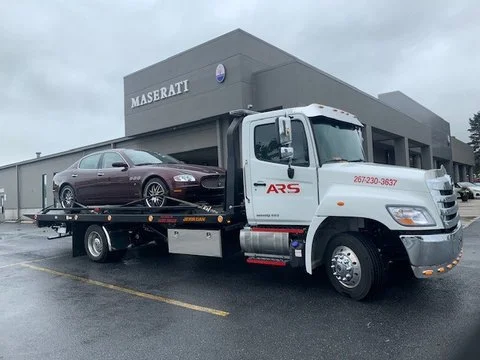 Flatbed tow truck parked outside Mason Maserati dealership, with a purple sedan loaded on the truck bed.