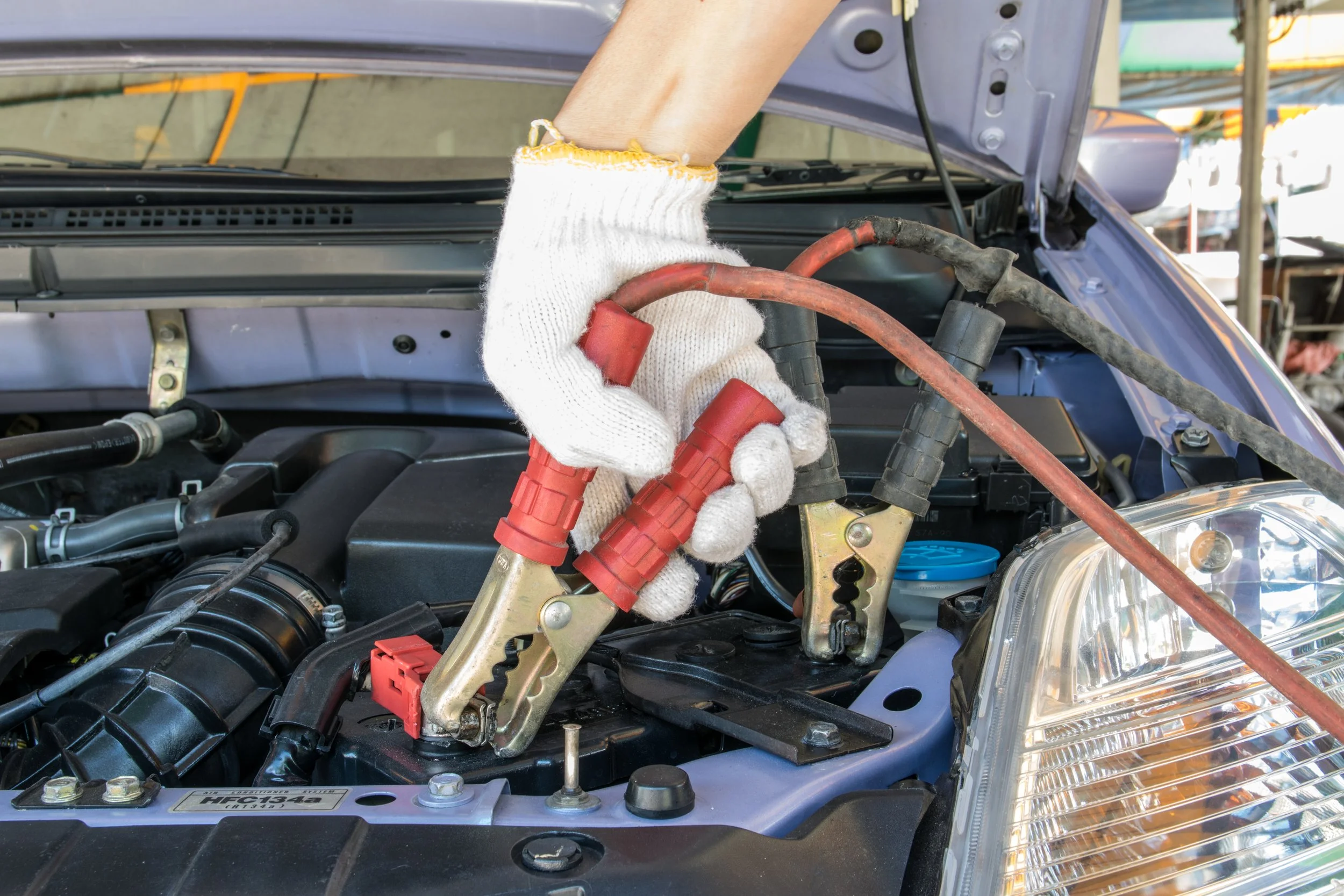 Person wearing white gloves using jumper cables to start a car with the hood open.