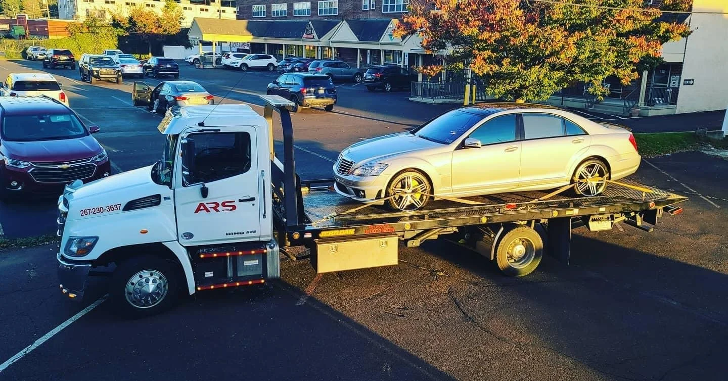 ARS Towing flatbed tow truck transporting a luxury sedan.