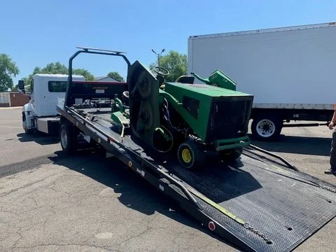 A flatbed tow truck carrying a green lawnmower.