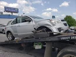 A silver sedan with a damaged front end is on a tow truck.