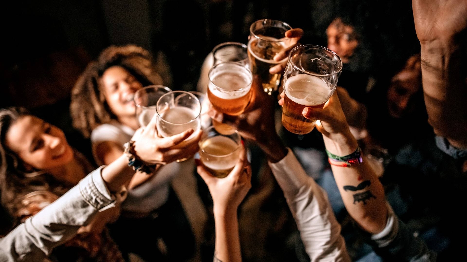 Group of friends raising glasses of beer in a toast at a party.