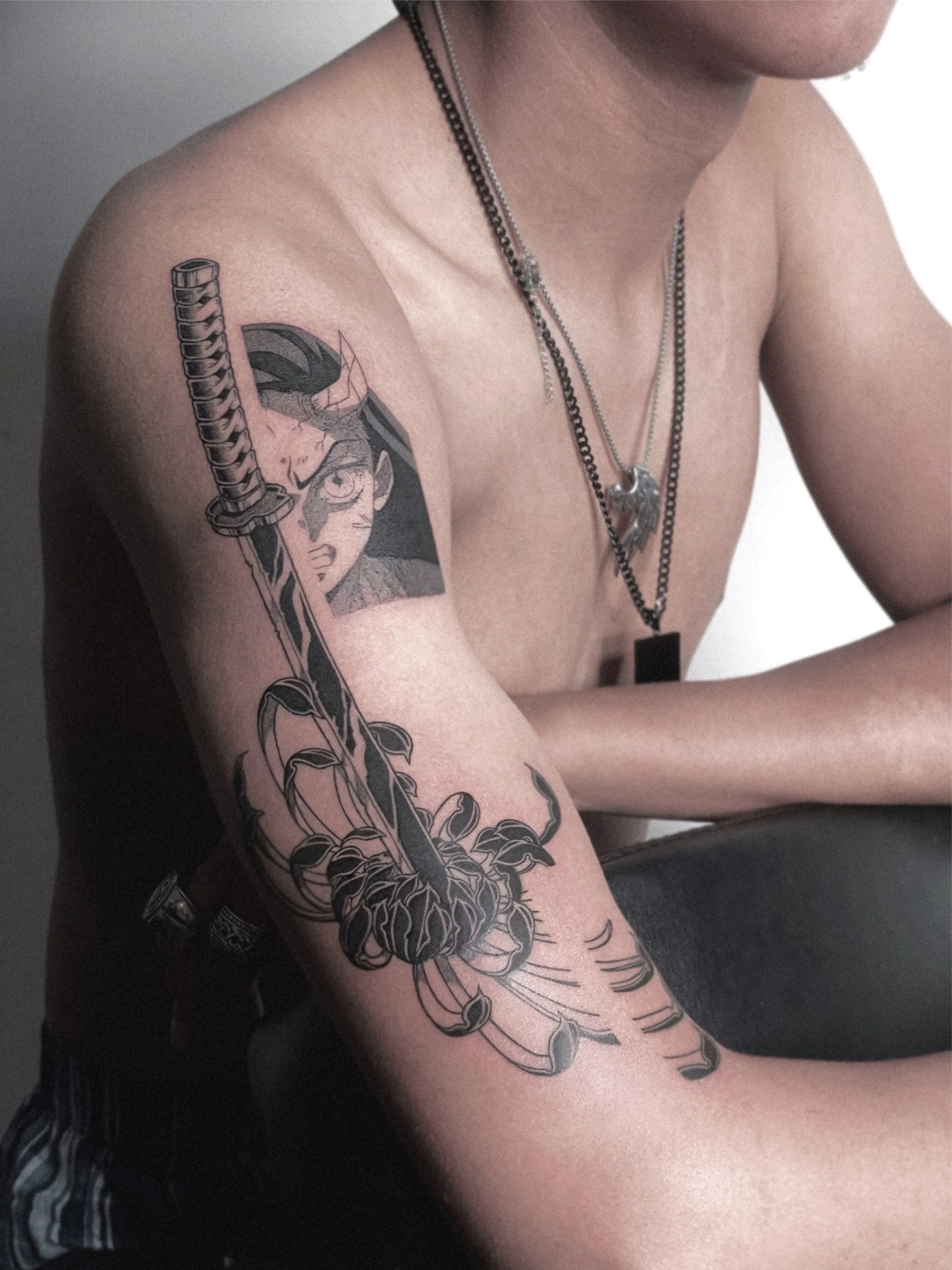 Tattoo of a female anime character with a katana on a person's upper arm, featuring black and gray shading.