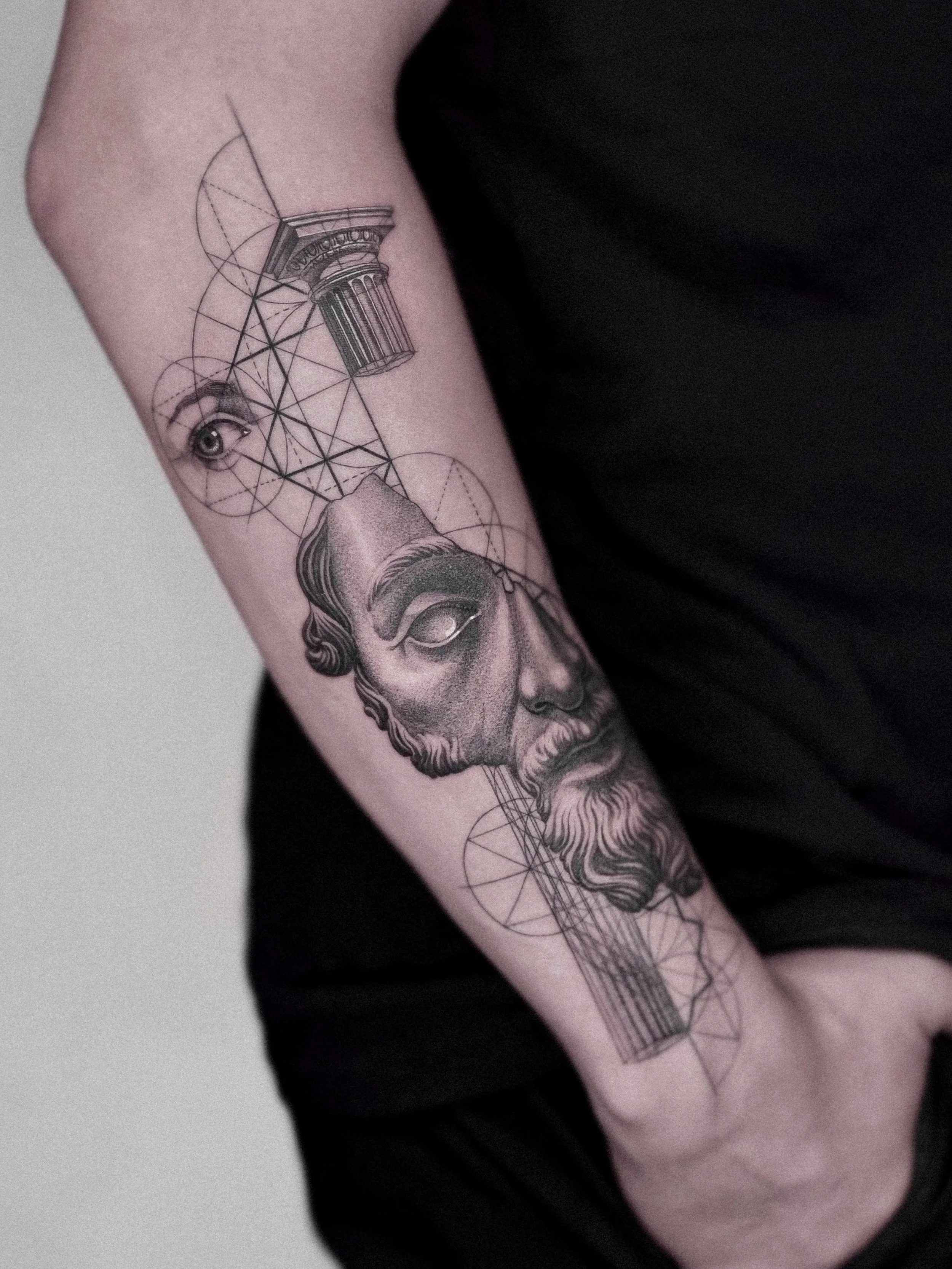 Tattoo of a classical Greek statue head with geometric lines and architectural elements on the arm.