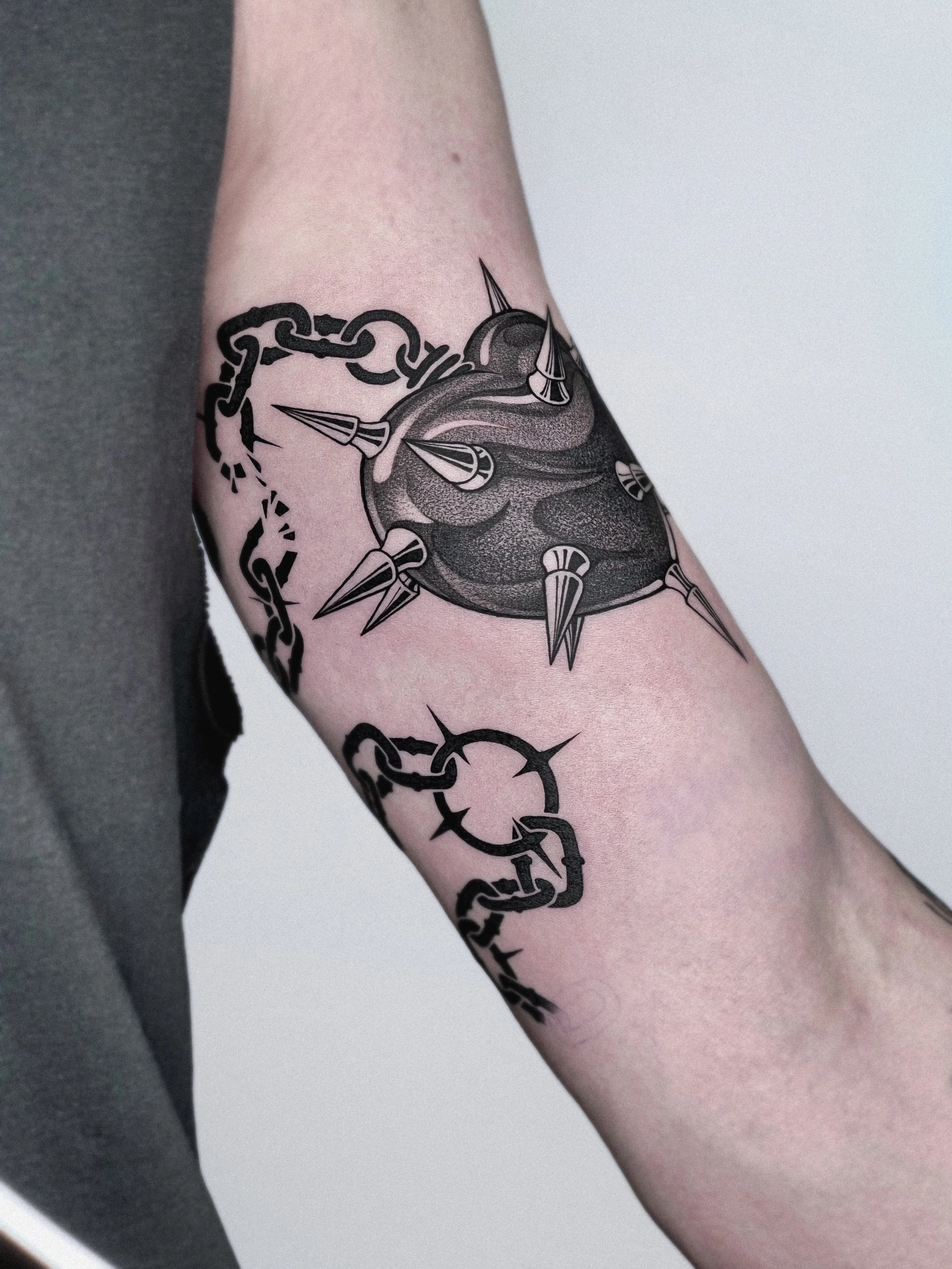 A tattoo of a spiked, metal ball chain design on a person's upper arm by Dmytro Shcherbakov