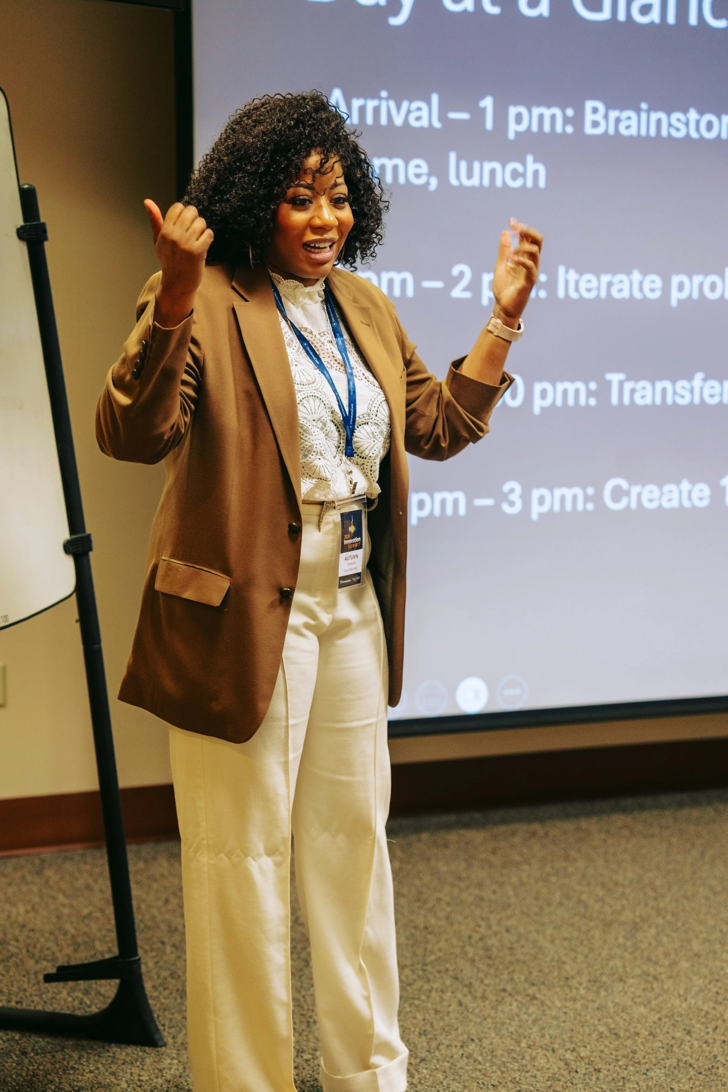 A woman giving a presentation in a conference room, standing in front of a large screen displaying an agenda with times and activities.