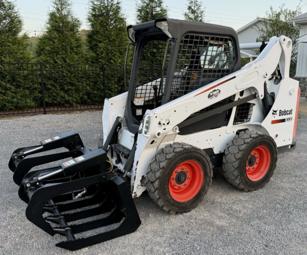 Skid steer loader with front grapple attachment and four-wheel drive for lifting and moving materials, available for rent at McKinleyville Ace Home & Garden Center.