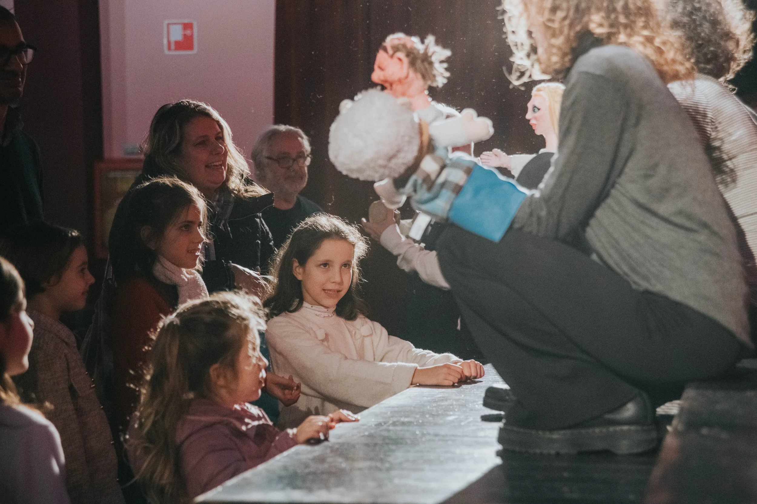 Un burattinaio mostra un burattino a un gruppo di bambini seduti davanti a un palco, scena di uno spettacolo di burattini.