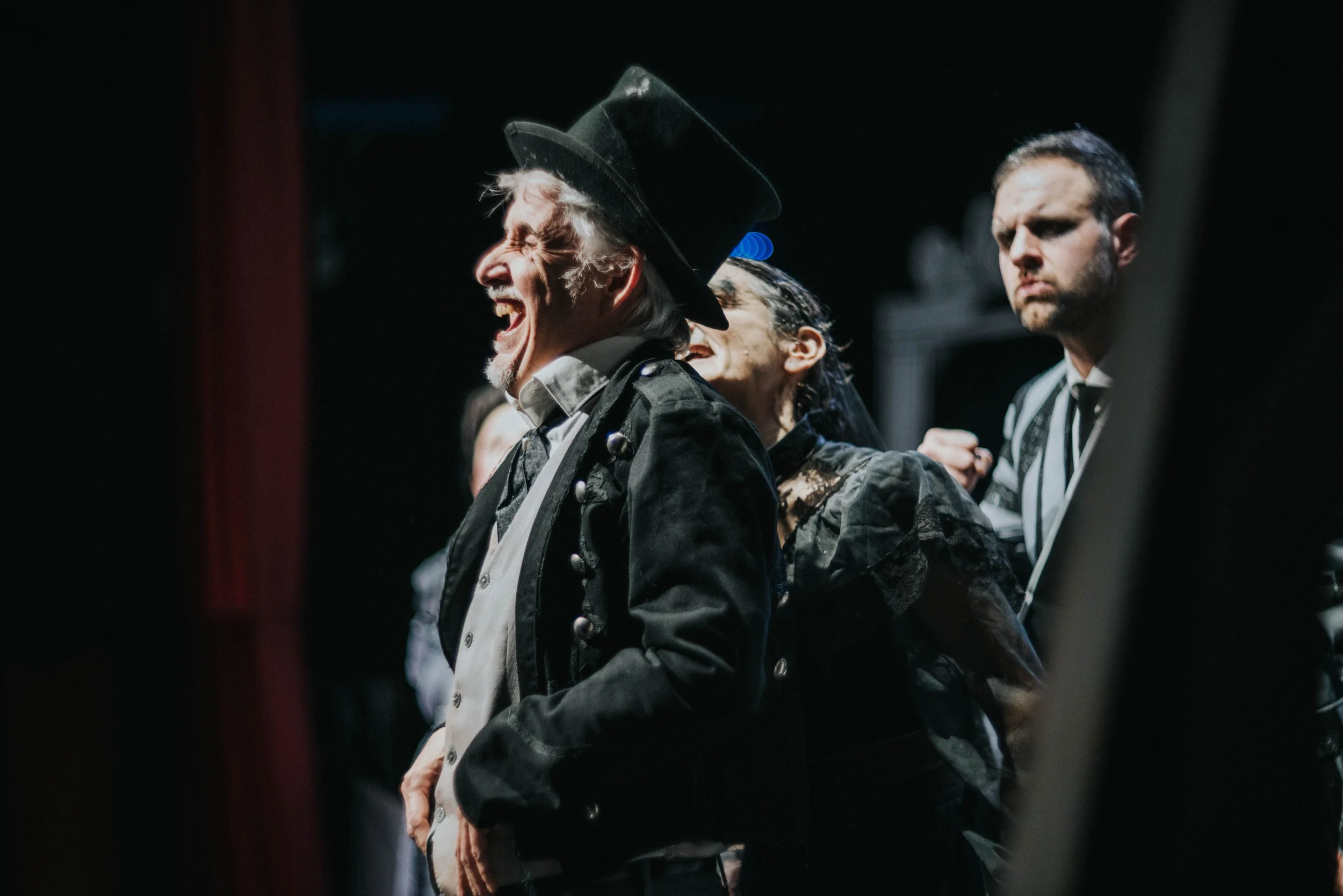 Persone vestite in abiti teatrali o storici, sorridenti e che ridono, in un ambiente scuro.