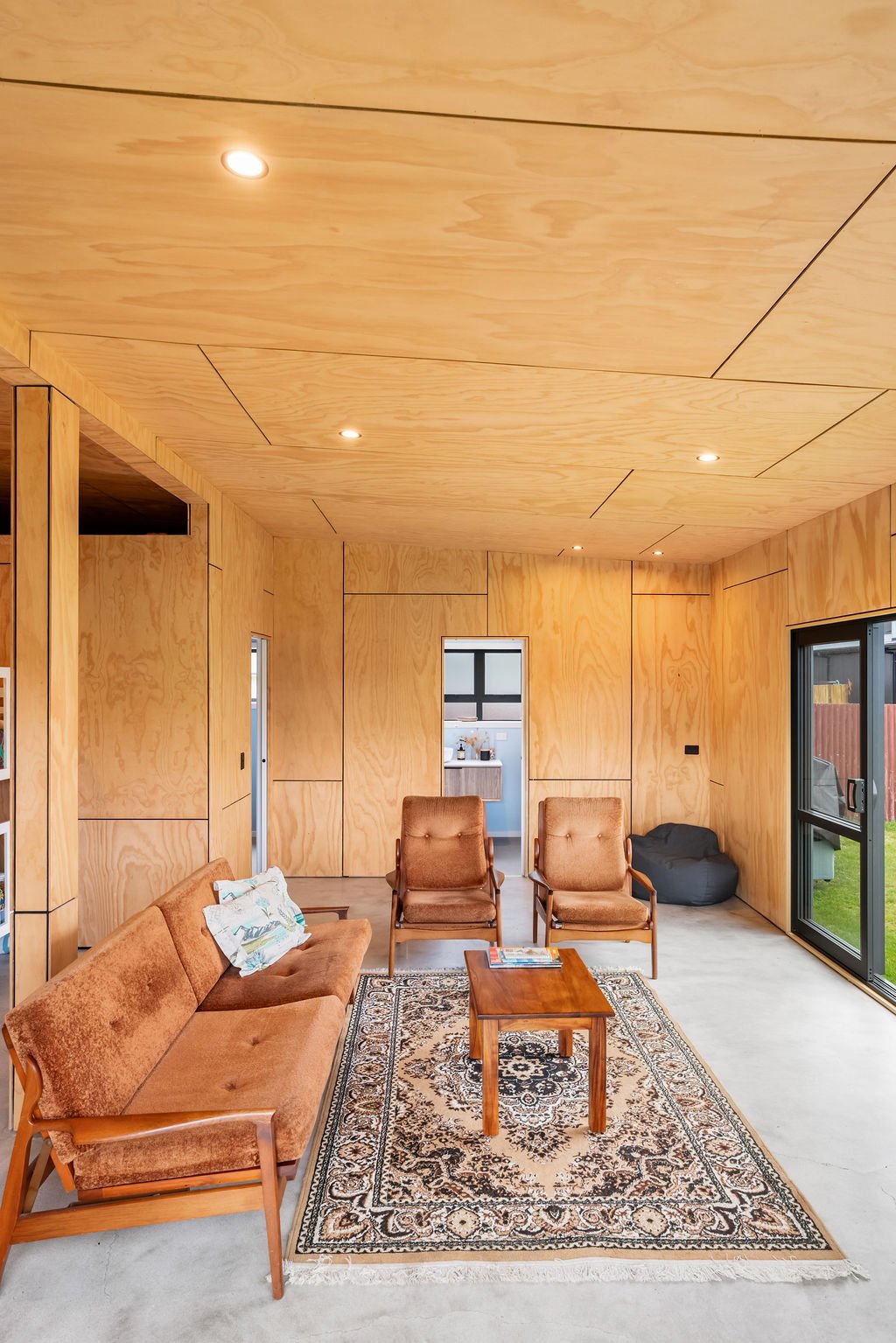 Living room with wooden paneling walls and ceiling, brown upholstered furniture, a wooden coffee table, an area rug, and sliding glass doors to the outside yard renovated by Zephyr Construction.