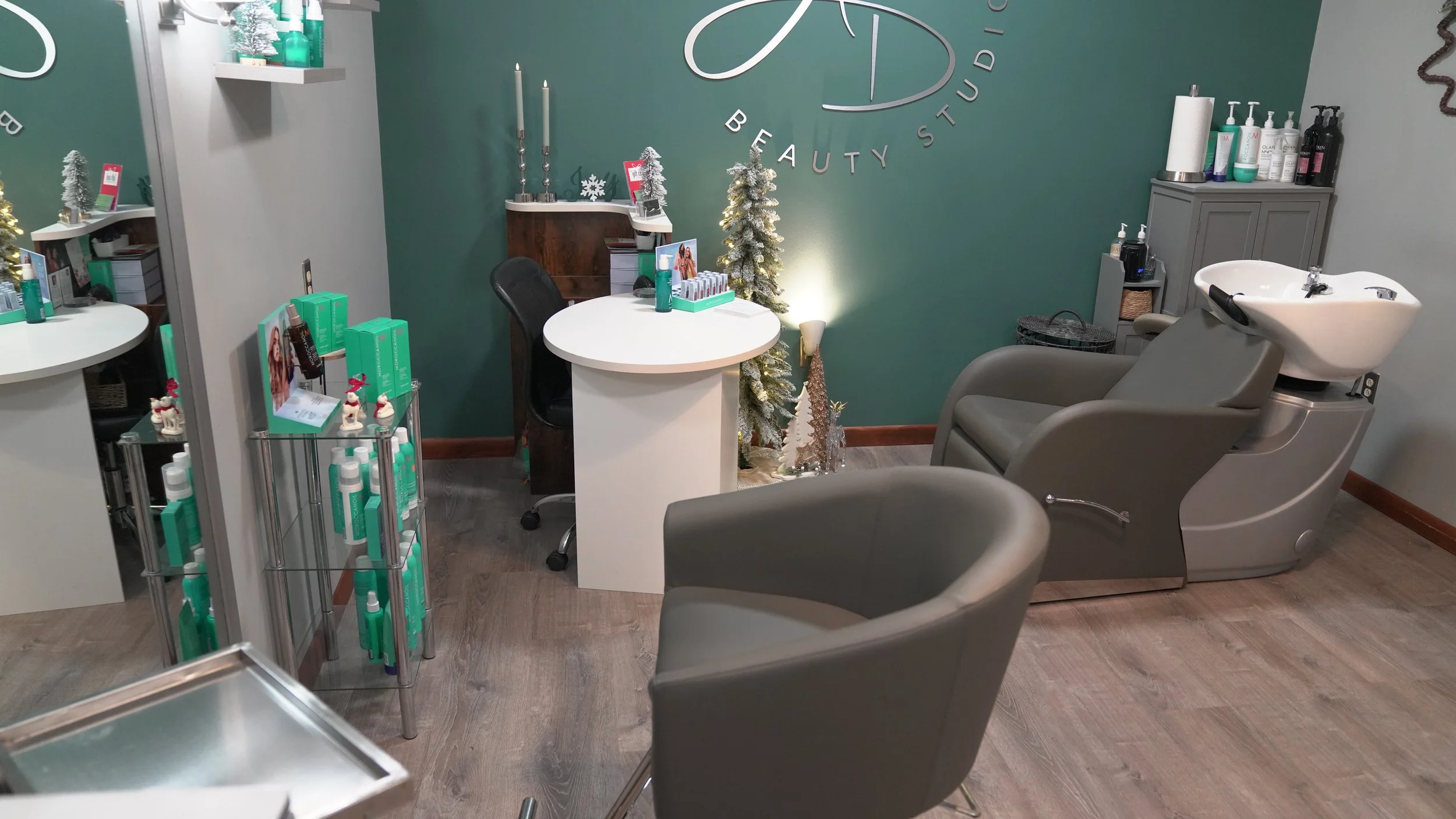 Beauty studio with a facial bed, a manicure station, and Christmas decorations, including a small snowy tree, in a cozy interior.