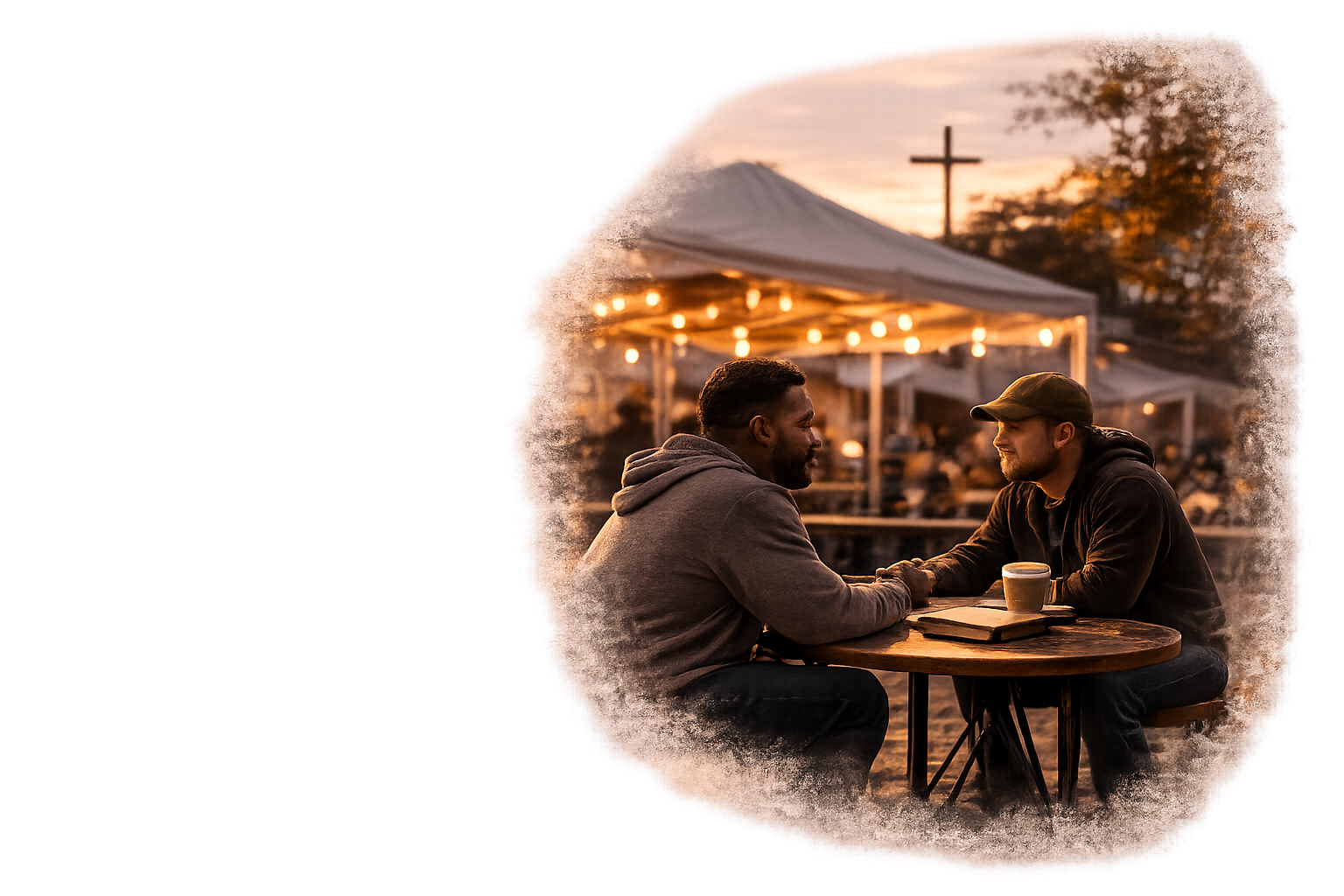 Two men sitting at a wooden table outdoors during sunset, holding hands and smiling at each other, with drinks and a notebook on the table, at a lively venue with string lights and a cross in the background.