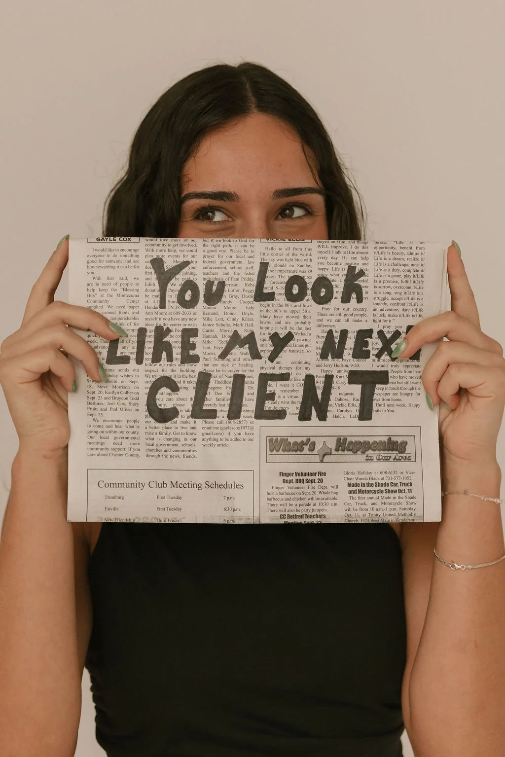 Woman holding up a newspaper with the words "You Look Like My Next Client" written in big black letters.