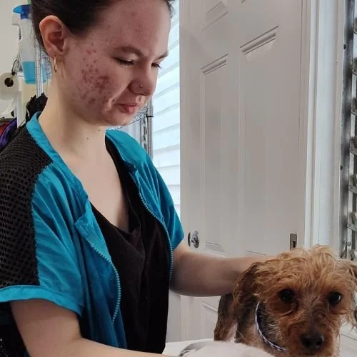 Young woman with acne on face holding a small brown dog with curly fur
