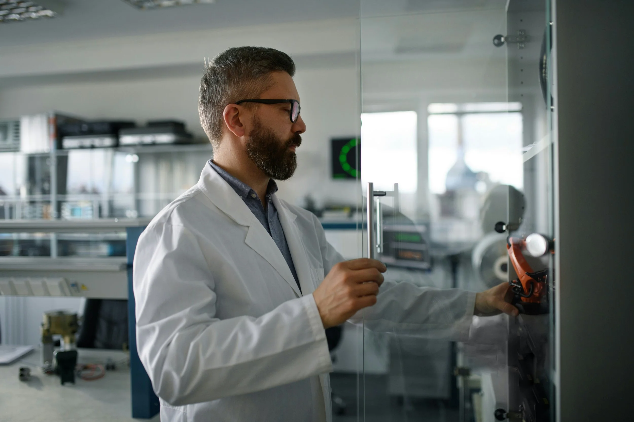 A scientist in a white lab coat adjusting equipment inside a laboratory.