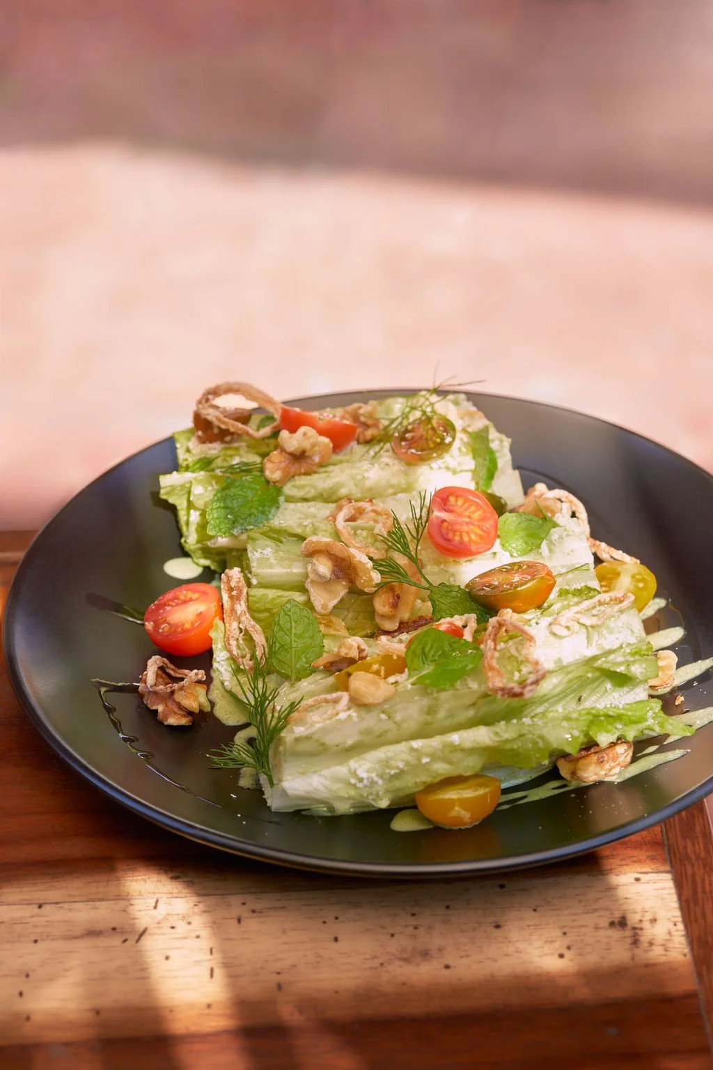 Ensalada con lechuga, tomates cherry, nueces, hojas de menta y eneldo, y aderezo cremoso en un plato negro.