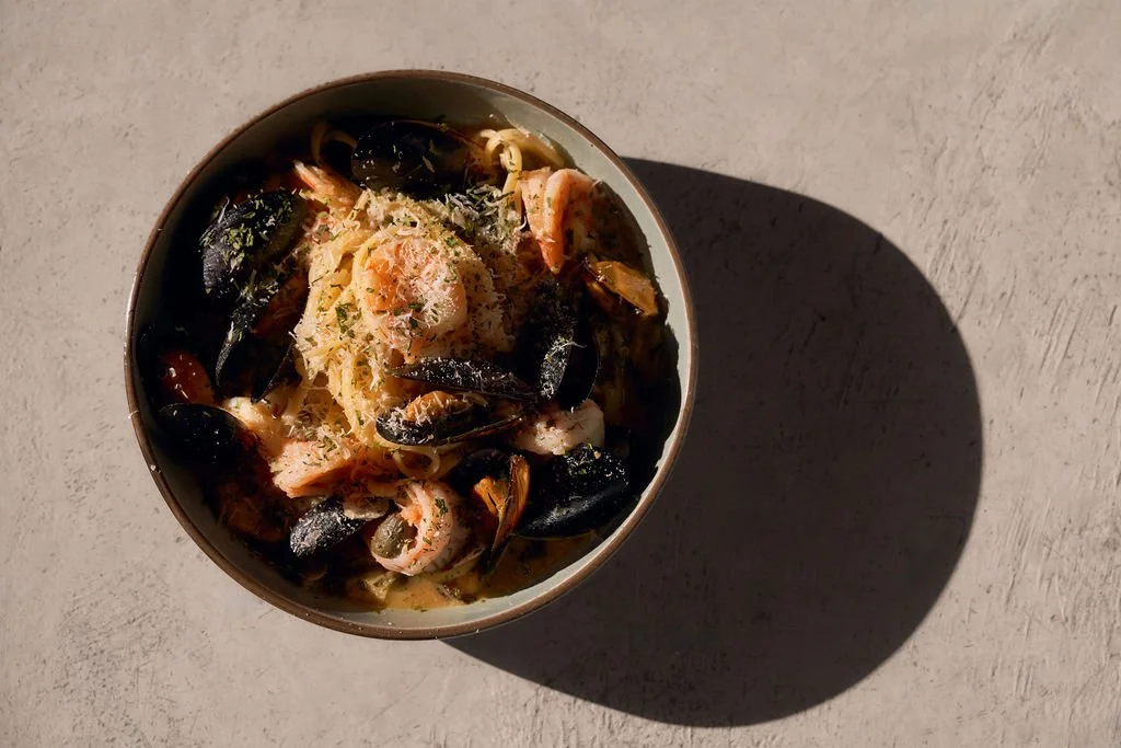 Plato de pasta con mariscos, calamares, mejillones y camarones, cubierto de queso rallado.
