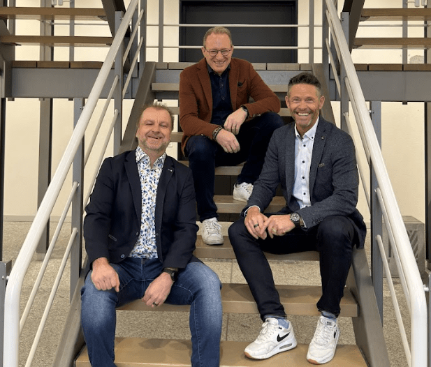 Drei Männer sitzen auf einer Treppe und lachen, im Hintergrund ein Treppengeländer.