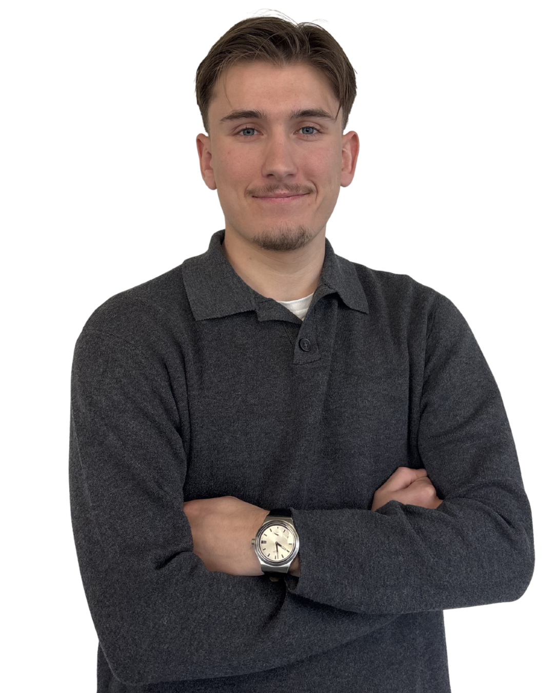 Jeune homme avec cheveux bruns, portant un pull gris foncé et une montre argentée, bras croisés, souriant légèrement.