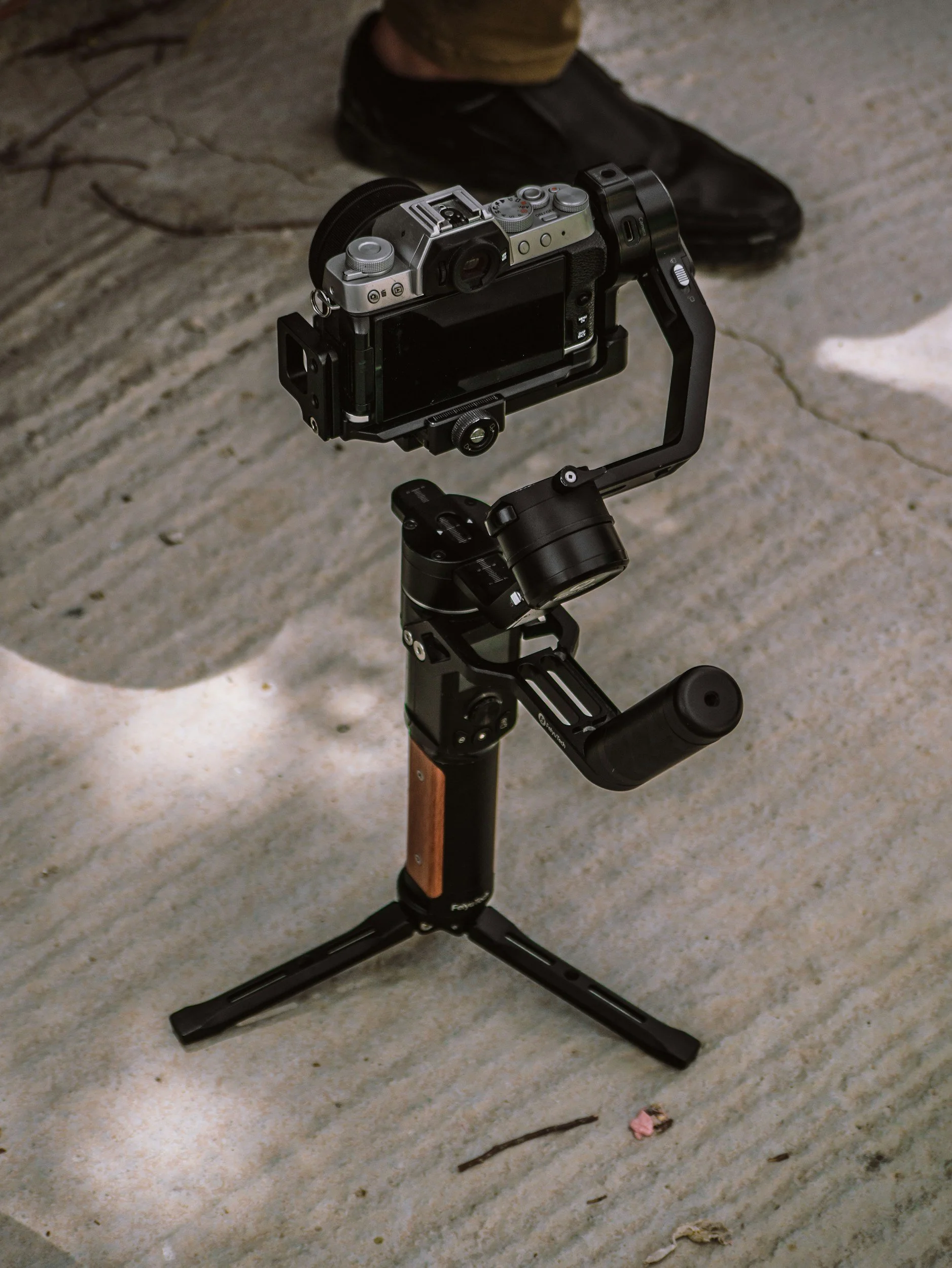 Camera on a stabilizer tripod on a concrete surface, with a person's shoe and pant leg visible in the background.