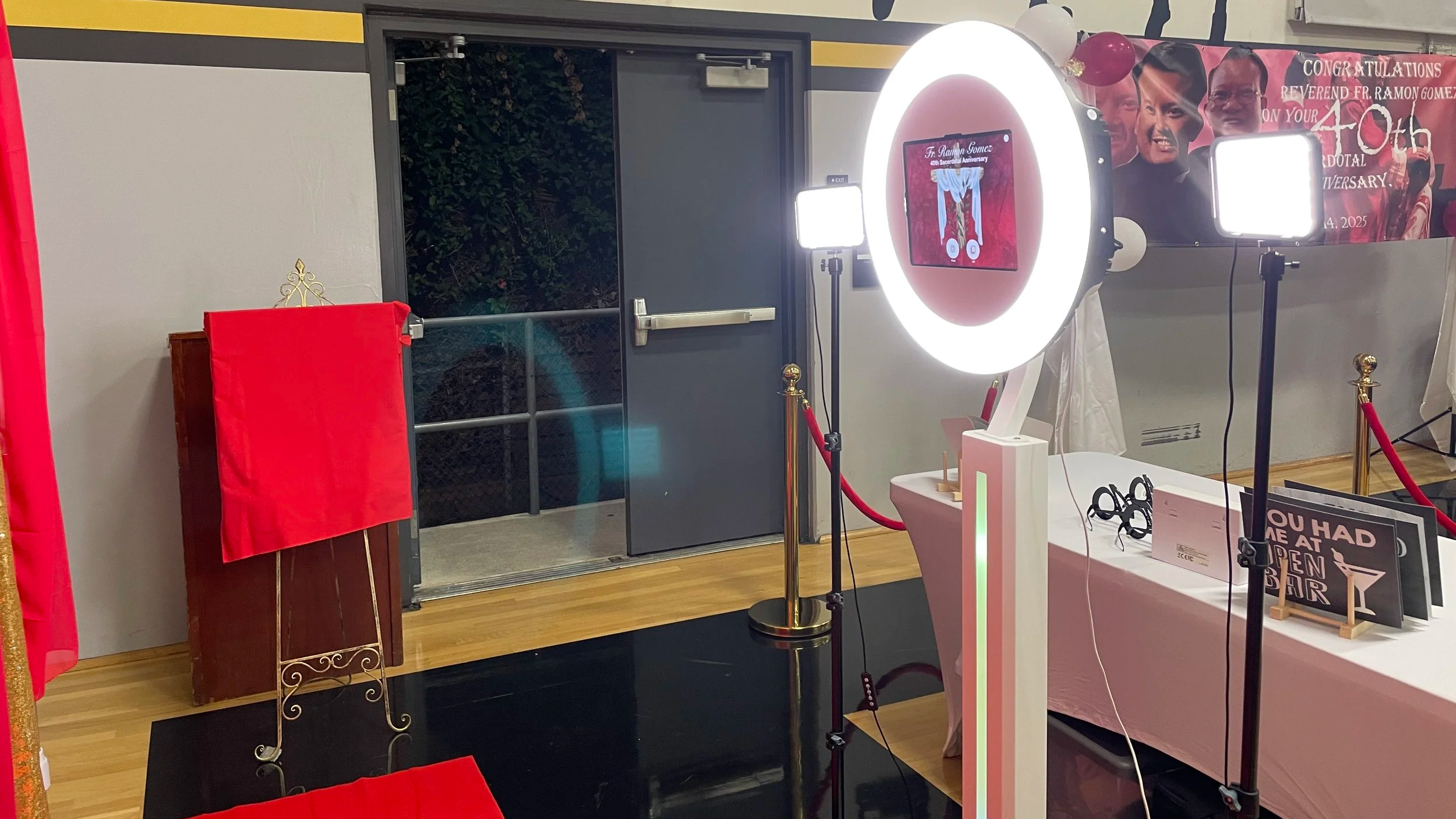 Photo studio setup with ring lights, a backdrop, and a sign celebrating a religious anniversary event.