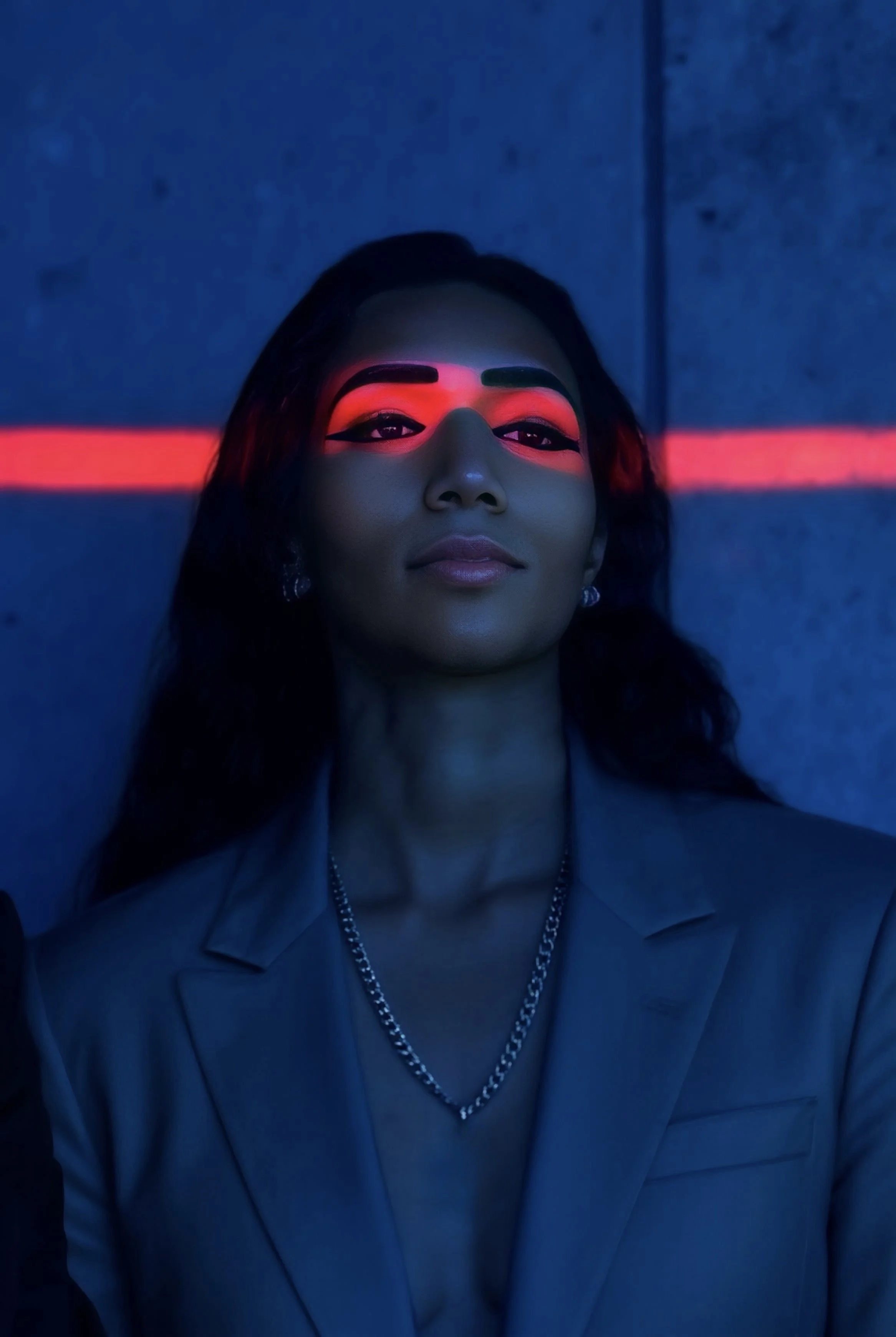 A woman with dark hair and makeup, illuminated by a red horizontal line across her face, against a dark background.
