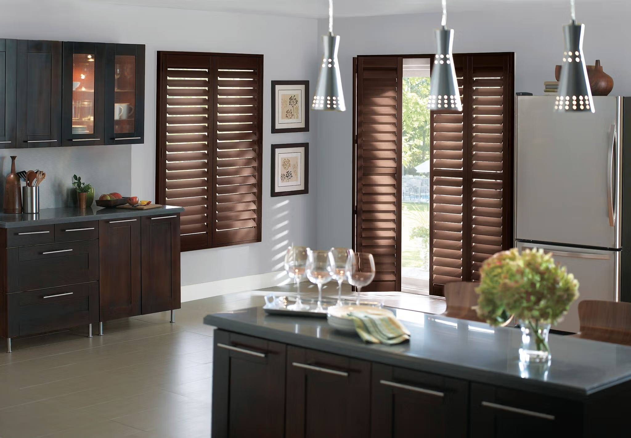 Modern kitchen with dark wooden cabinets, brown window shutters, and a gray island with glasses and a flower vase on it.