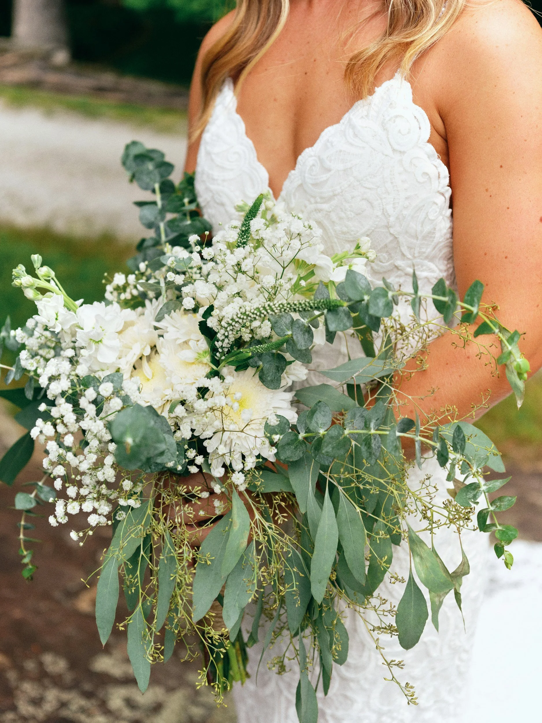 A woman on her wedding day holding a bouquet of white flowers and greenery, wearing a white lace wedding dress. Richmond wedding planner and wedding planning services.Charlottesville wedding planner and wedding planning services.