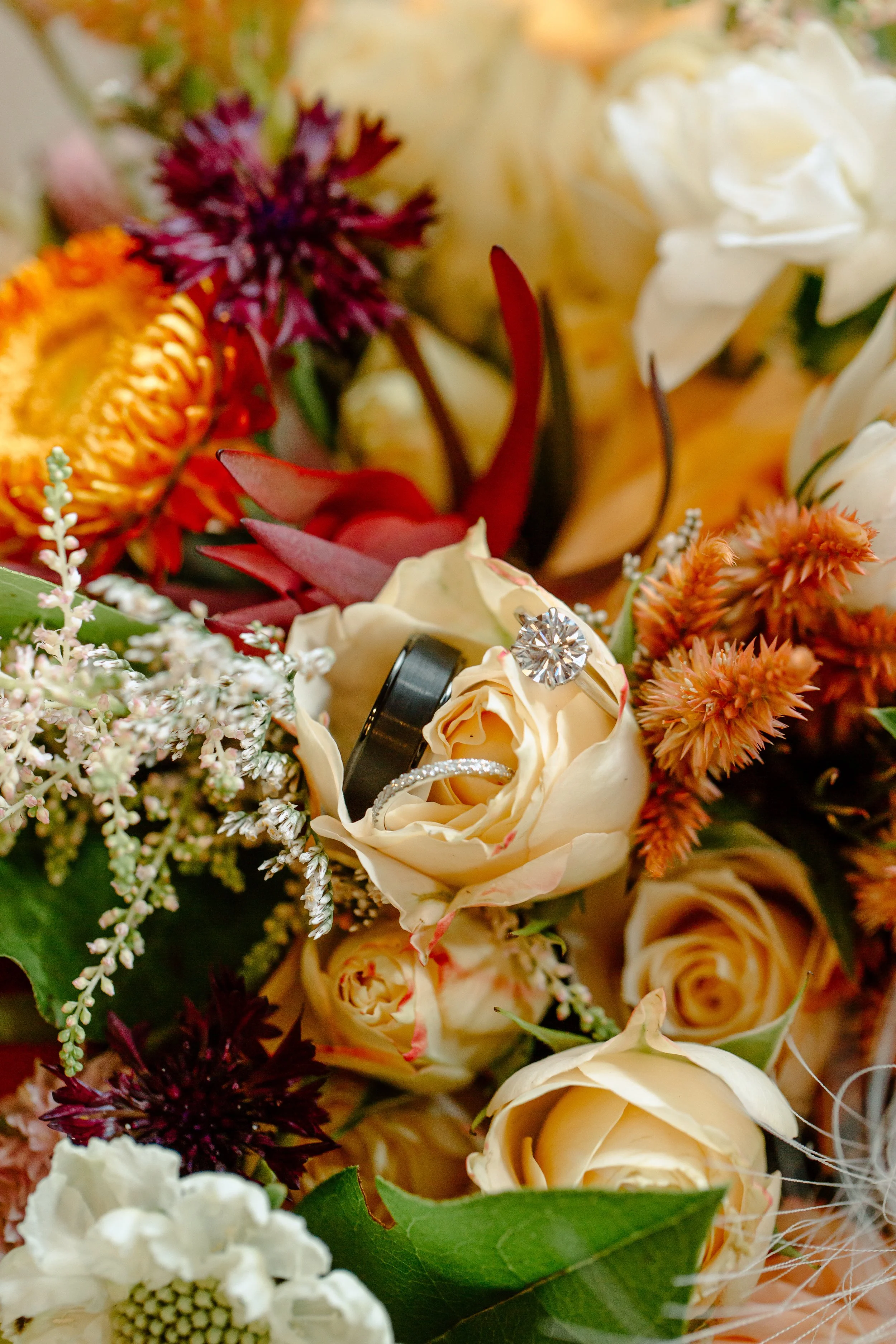 Close-up of wedding rings resting on a flower arrangement with roses and various colorful flowers.