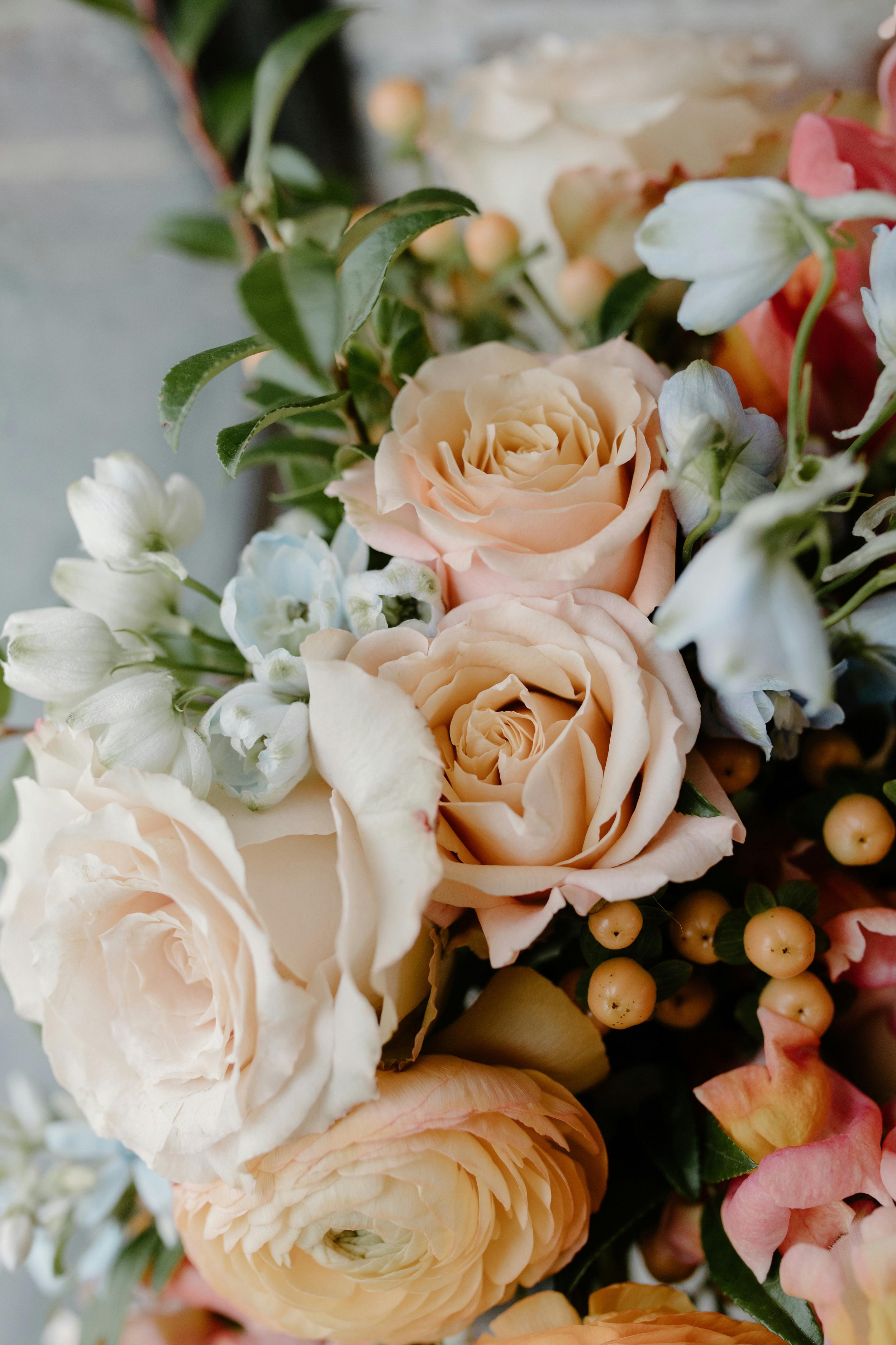 Close-up of a bridal bouquet of flowers with cream-colored roses, white and light blue flowers, and small orange berries.Charlottesville wedding planner wedding planning services. Richmond Wedding planning services