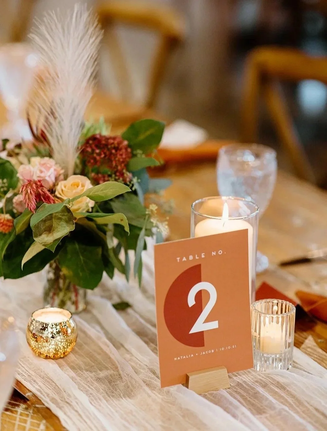 A table decorated with a floral centerpiece, candles, and a card indicating table number 2 at a wedding or event.