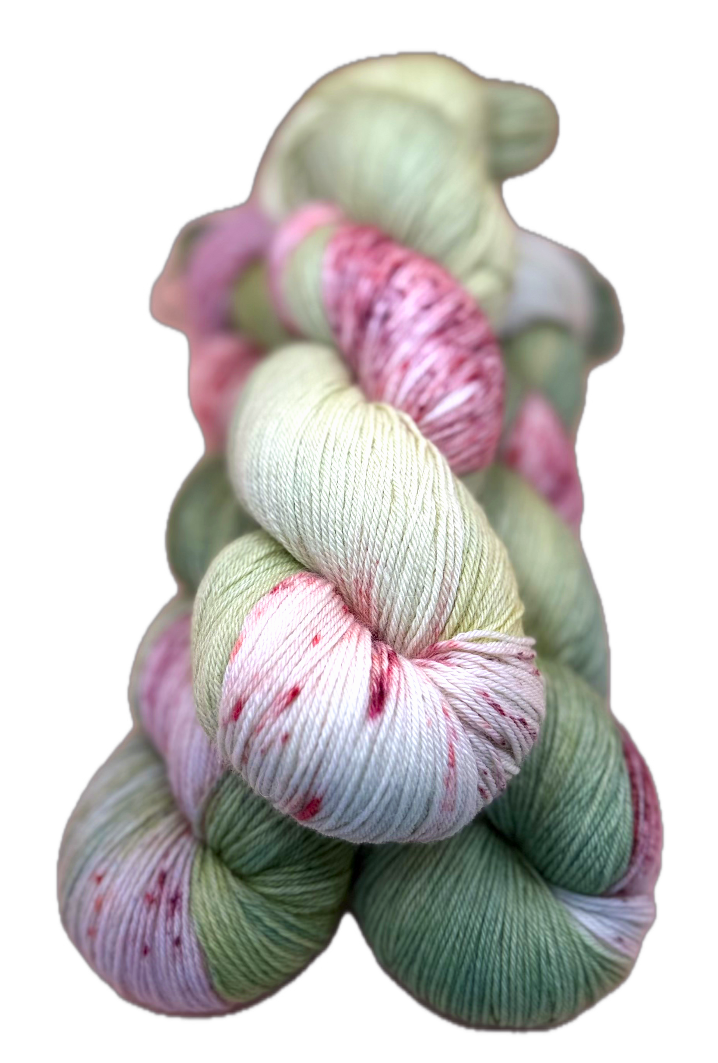 A twisted skein of hand dyed yarn, mostly green, pink, and white, with some speckles of darker pink and red.
