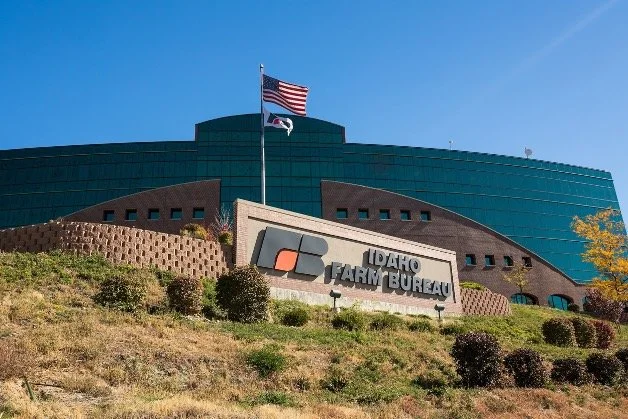 Front view of the Idaho Farm Bureau building with a sign, American flag, and blue sky.