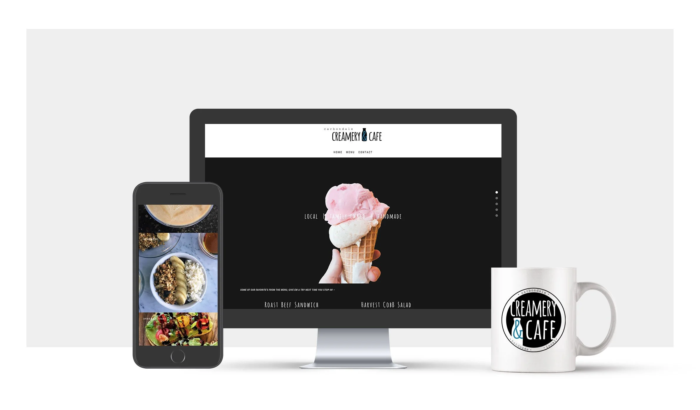 A computer monitor displays a website for Creamery & Cafe with an image of a hand holding a pink and white ice cream cone. A smartphone shows pictures of food, and a white coffee mug with the Creamery & Cafe logo is placed next to the monitor.