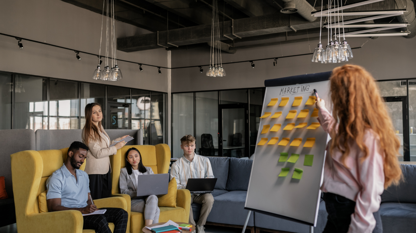 A marketing professional giving a presentation in an agency with other marketers strategizing on business marketing tactics and requirements
