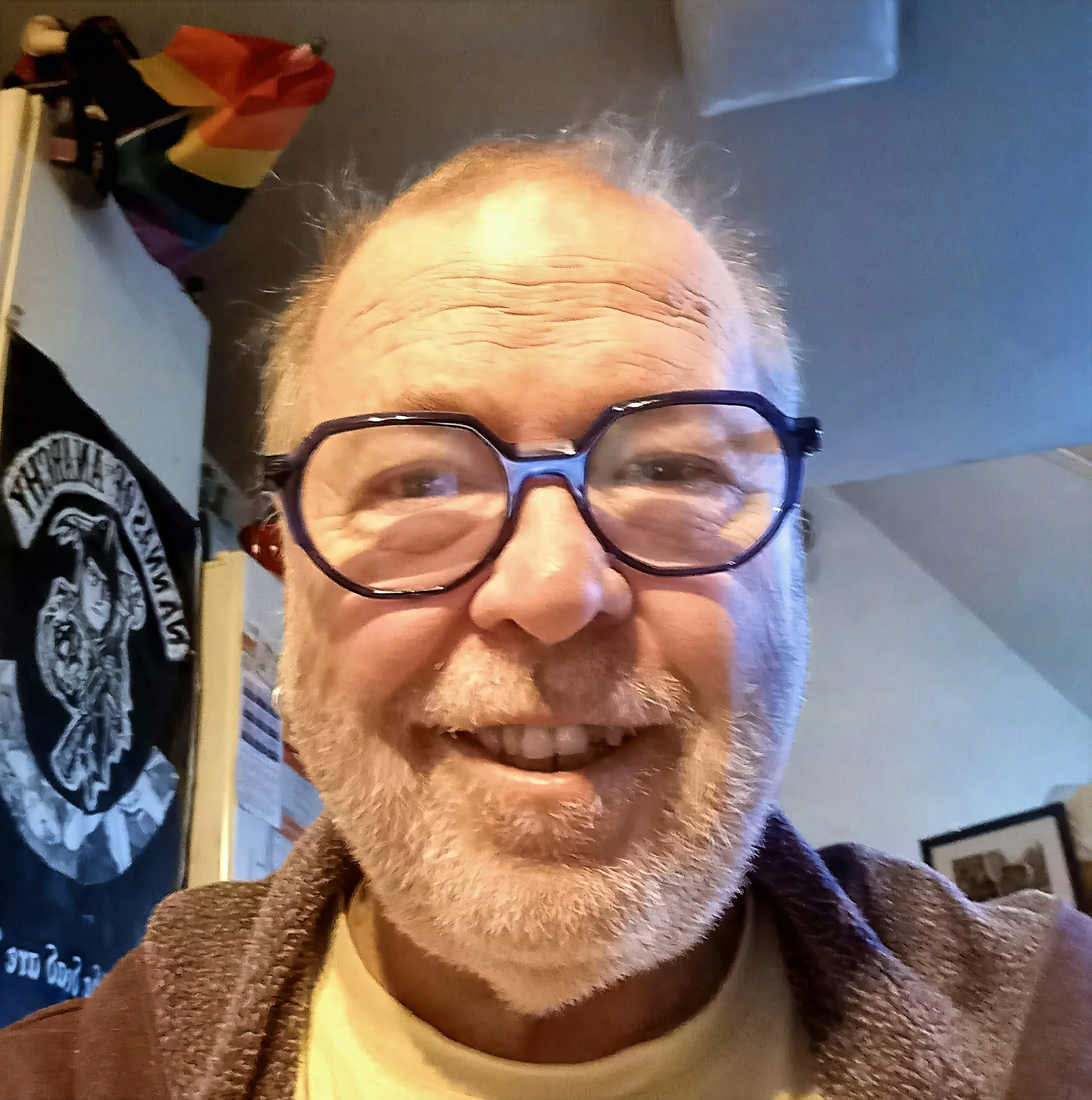 Close-up of a man's face with glasses, showing prominent wrinkles on his forehead and a warm smile.