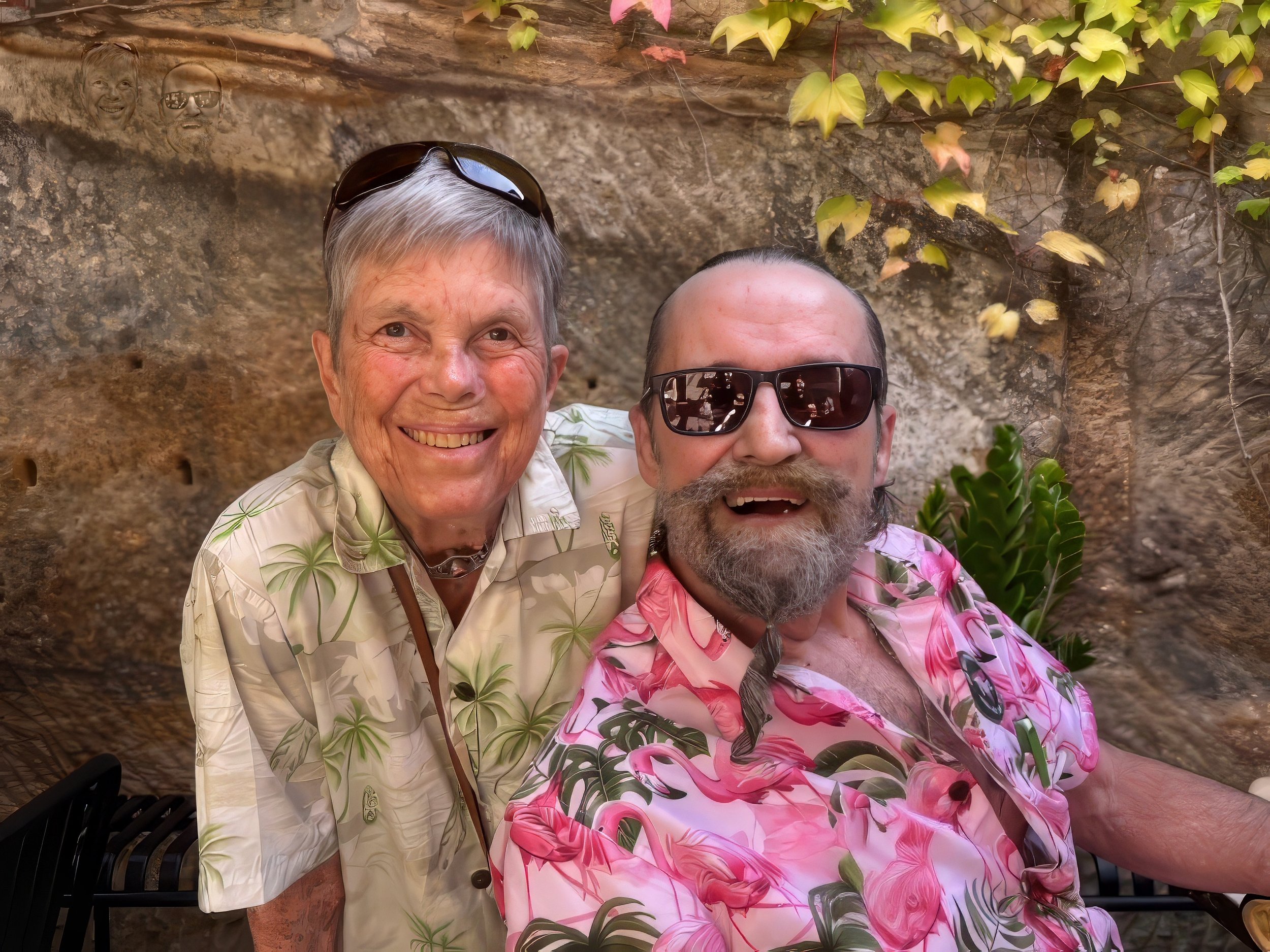 Two smiling men in Hawaiian shirts taking a selfie outdoors with a rocky and leafy background.