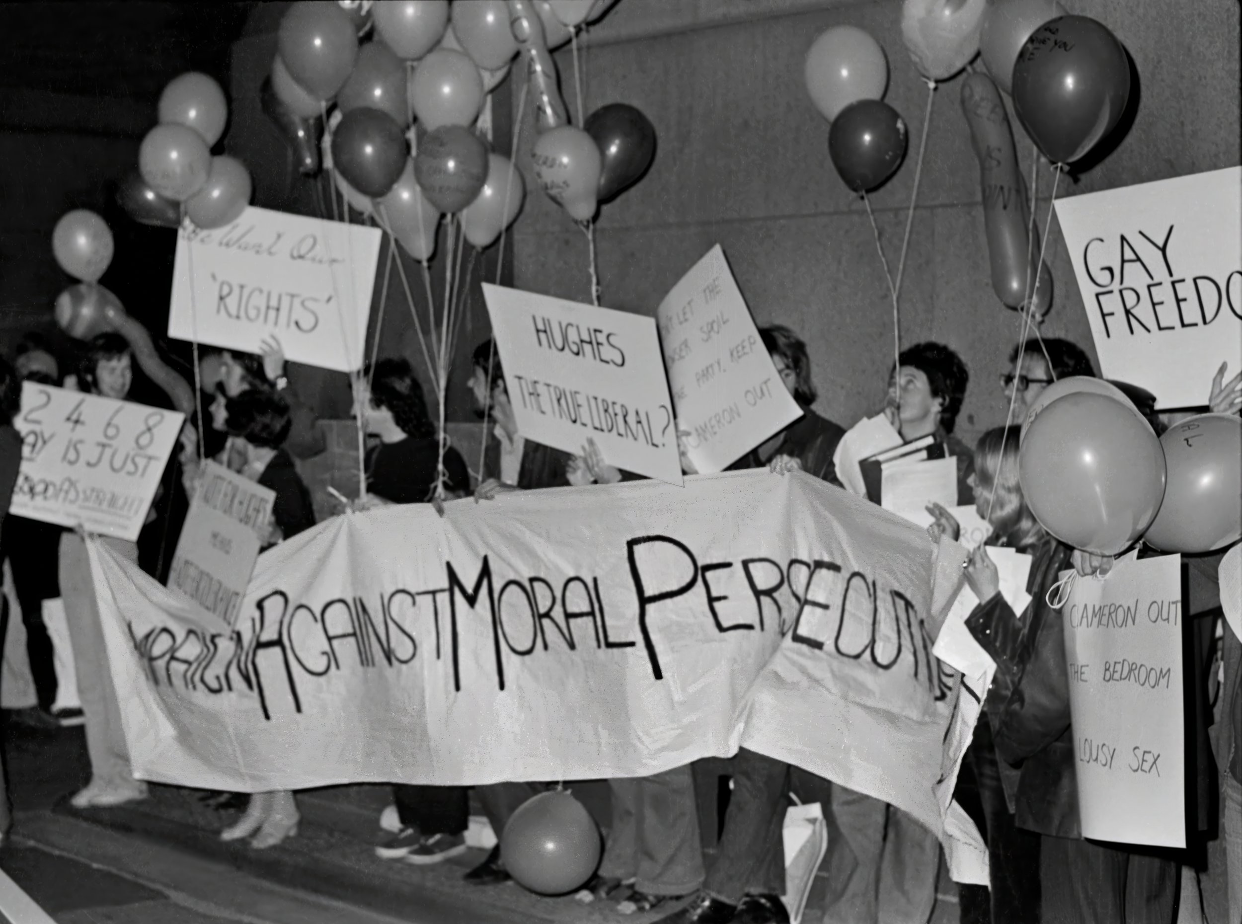 A crowd of people holding protest signs and balloons during a demonstration, with various signs advocating for rights and freedoms, including one prominent sign saying 'Resist Moderate People'.