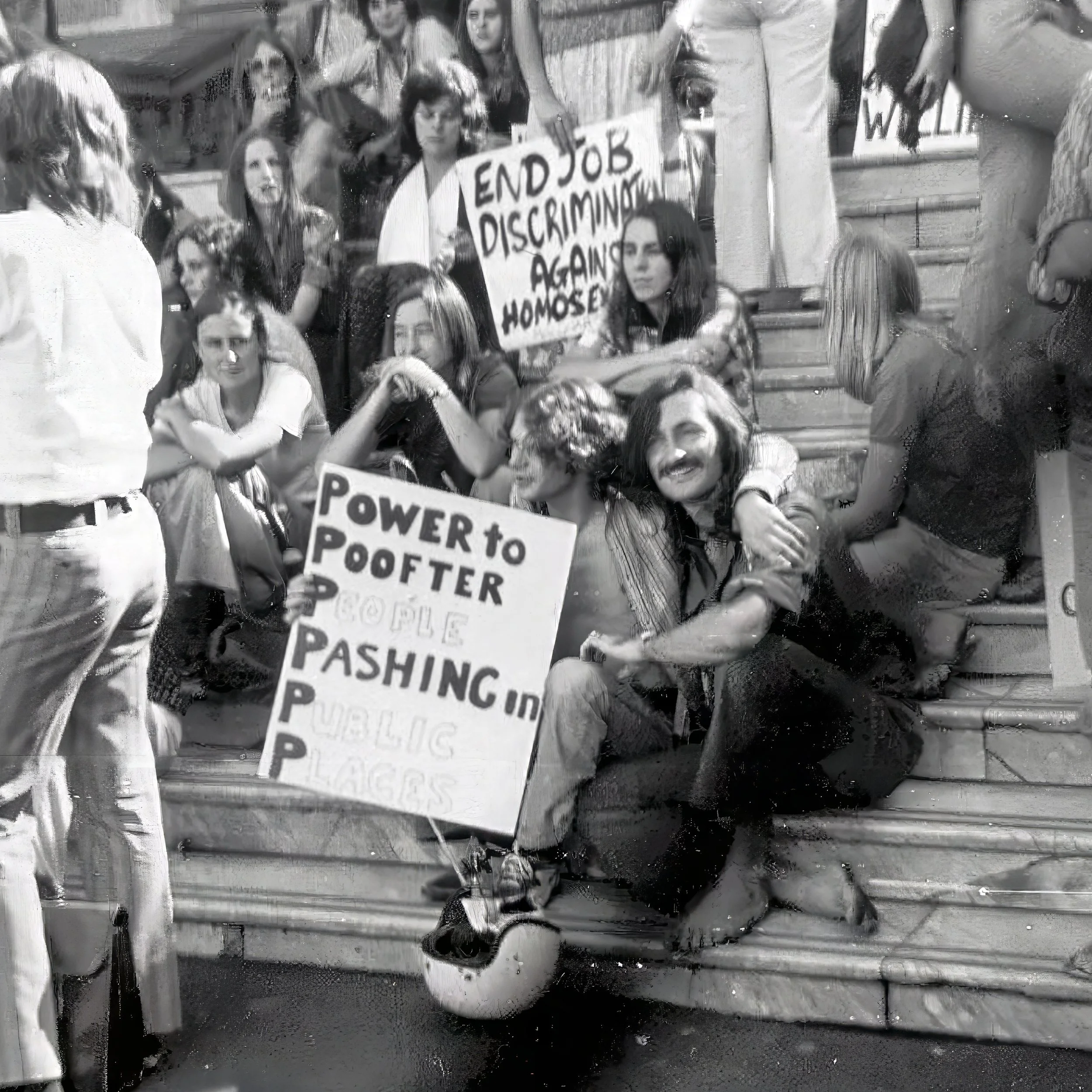 A group of people participating in a protest or march, holding signs. One sign says 'END JOB DISCRIMINATION AGAINST HOMOSEXUALS' and another says 'POWER TO THE PEOPLE.' The photo appears to be taken through a rain-covered window, giving it a blurry appearance.