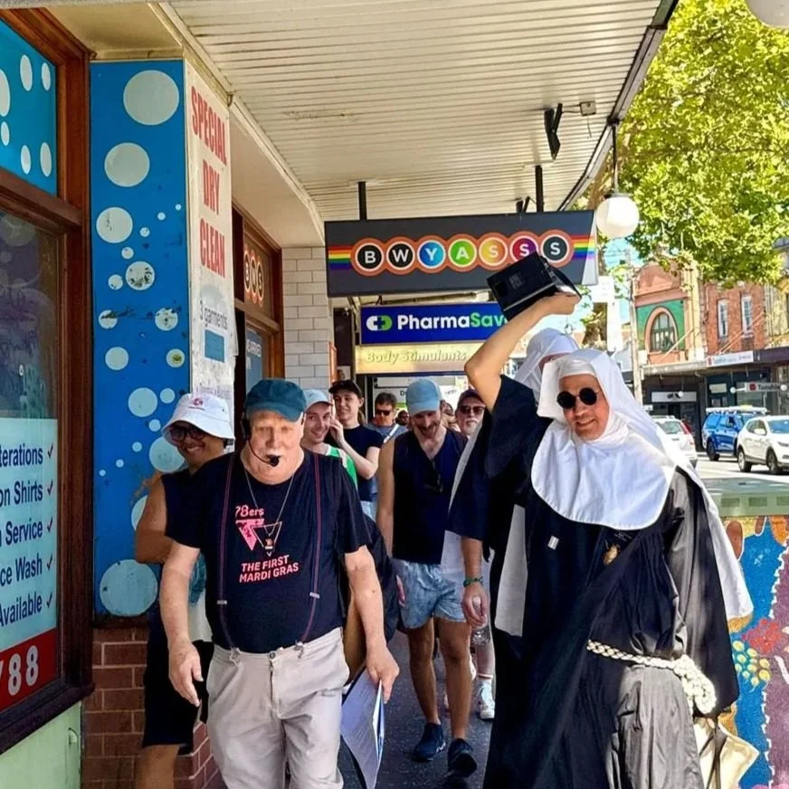 Group of people dressed in costumes walking outside a storefront on a sunny day.