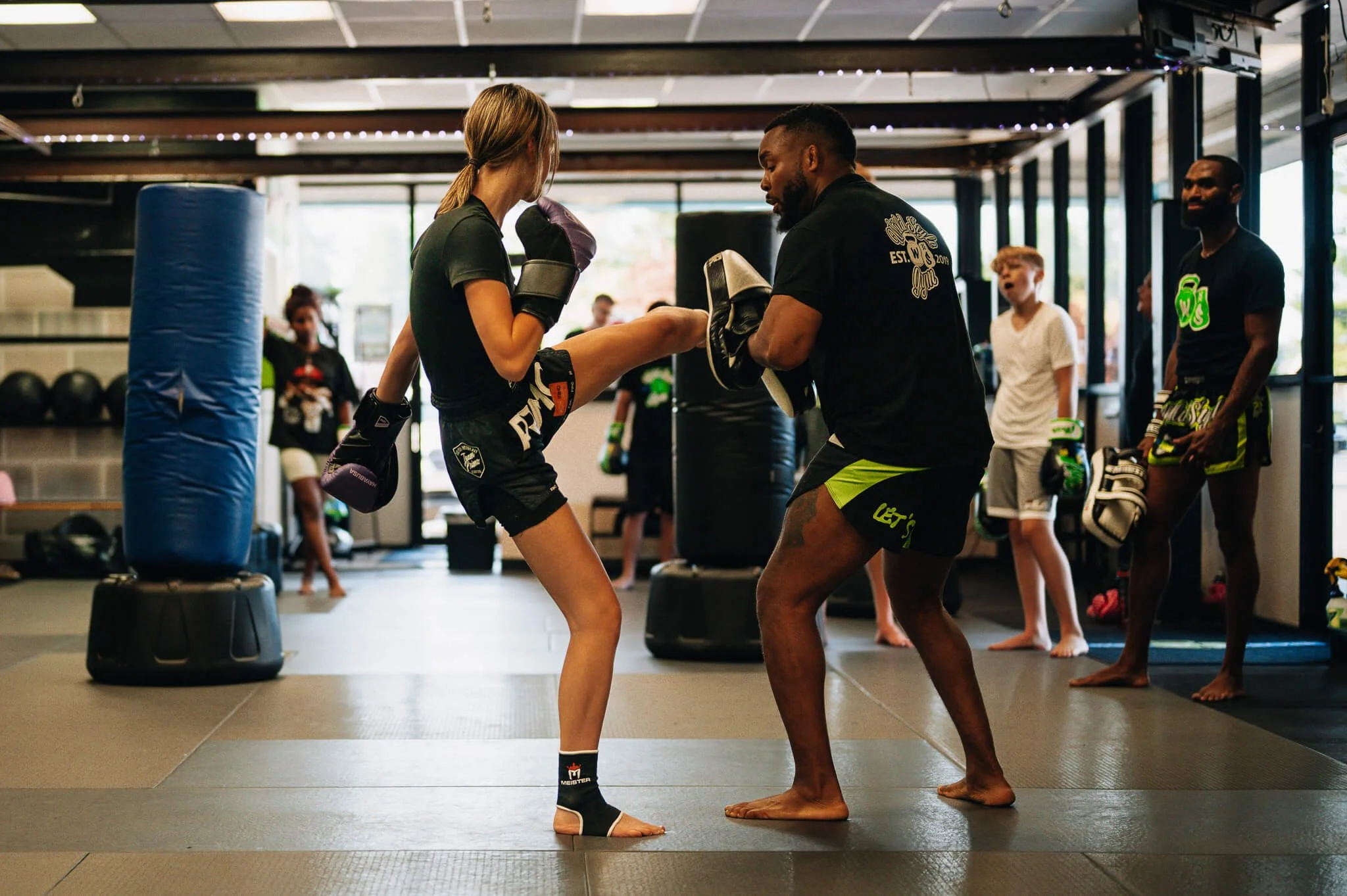 Adult freestyle kickboxing class at WildStyle Gym in Snohomish, WA, with a coach holding pads while a student practices controlled kicking technique.
