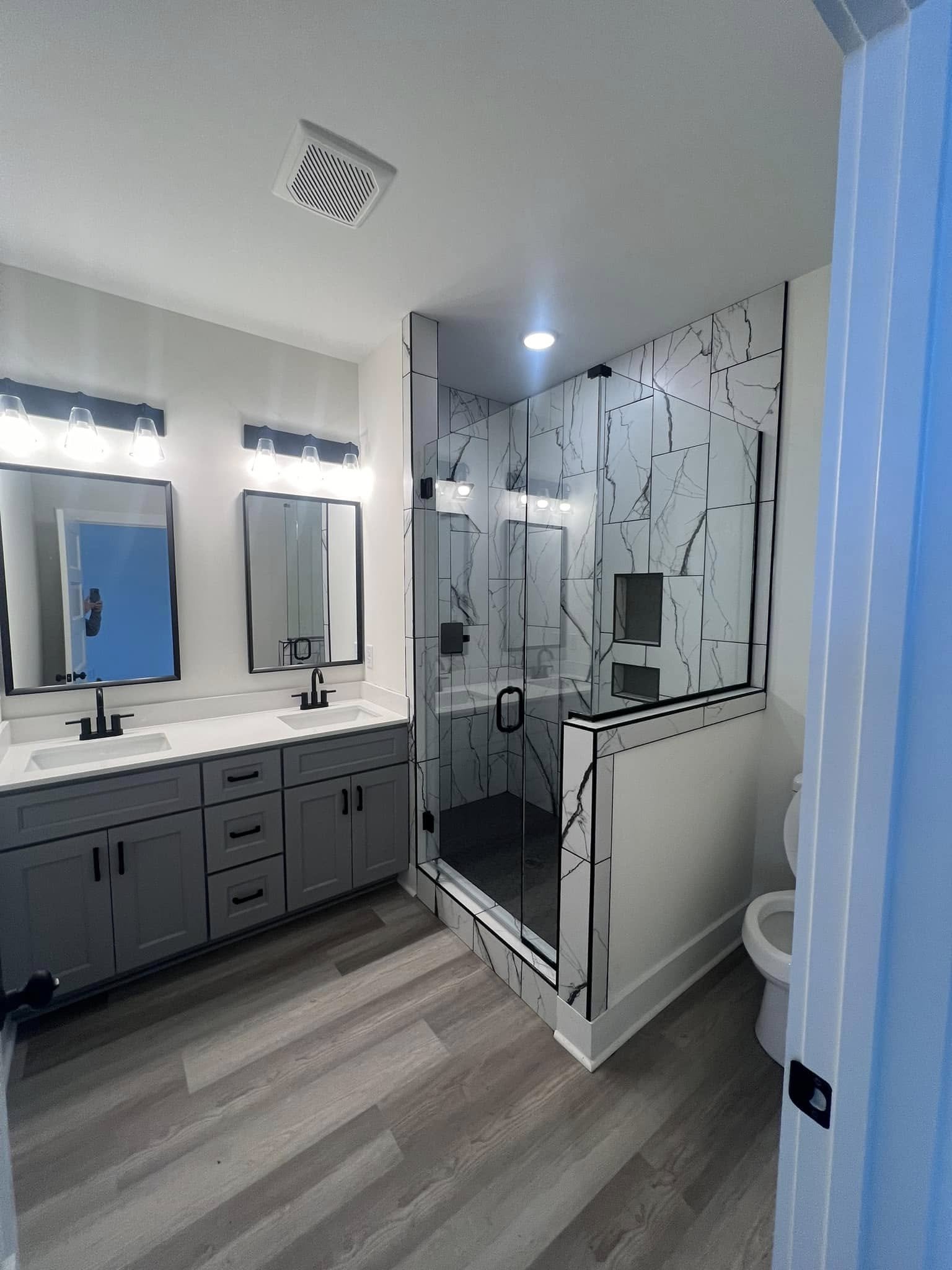 Modern bathroom with double vanity, black fixtures, and a glass-enclosed shower with marble tiles and built-in shelves.