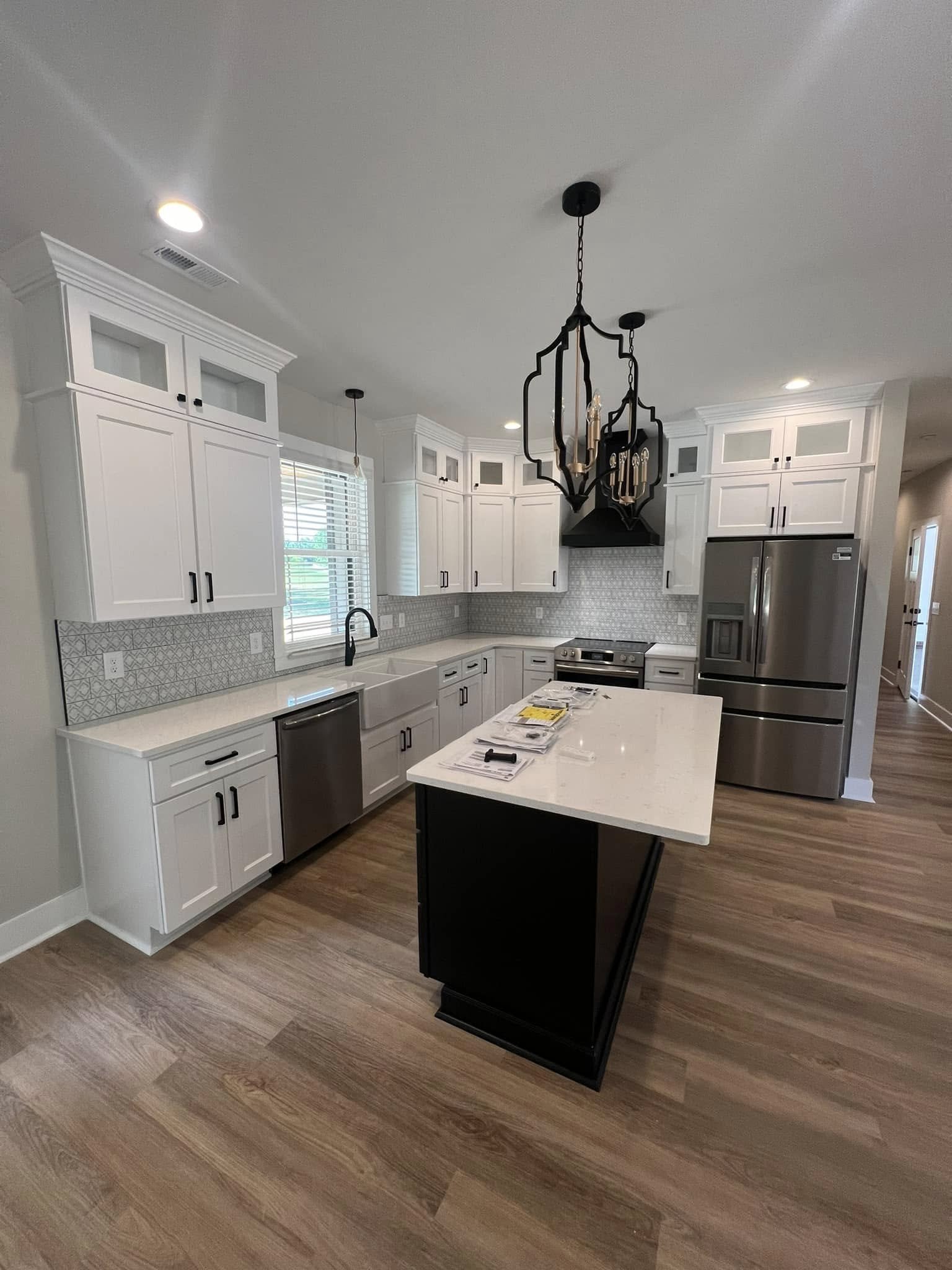Modern kitchen with white cabinetry, stainless steel appliances, a black island with a white countertop, and a decorative black chandelier hanging from the ceiling.