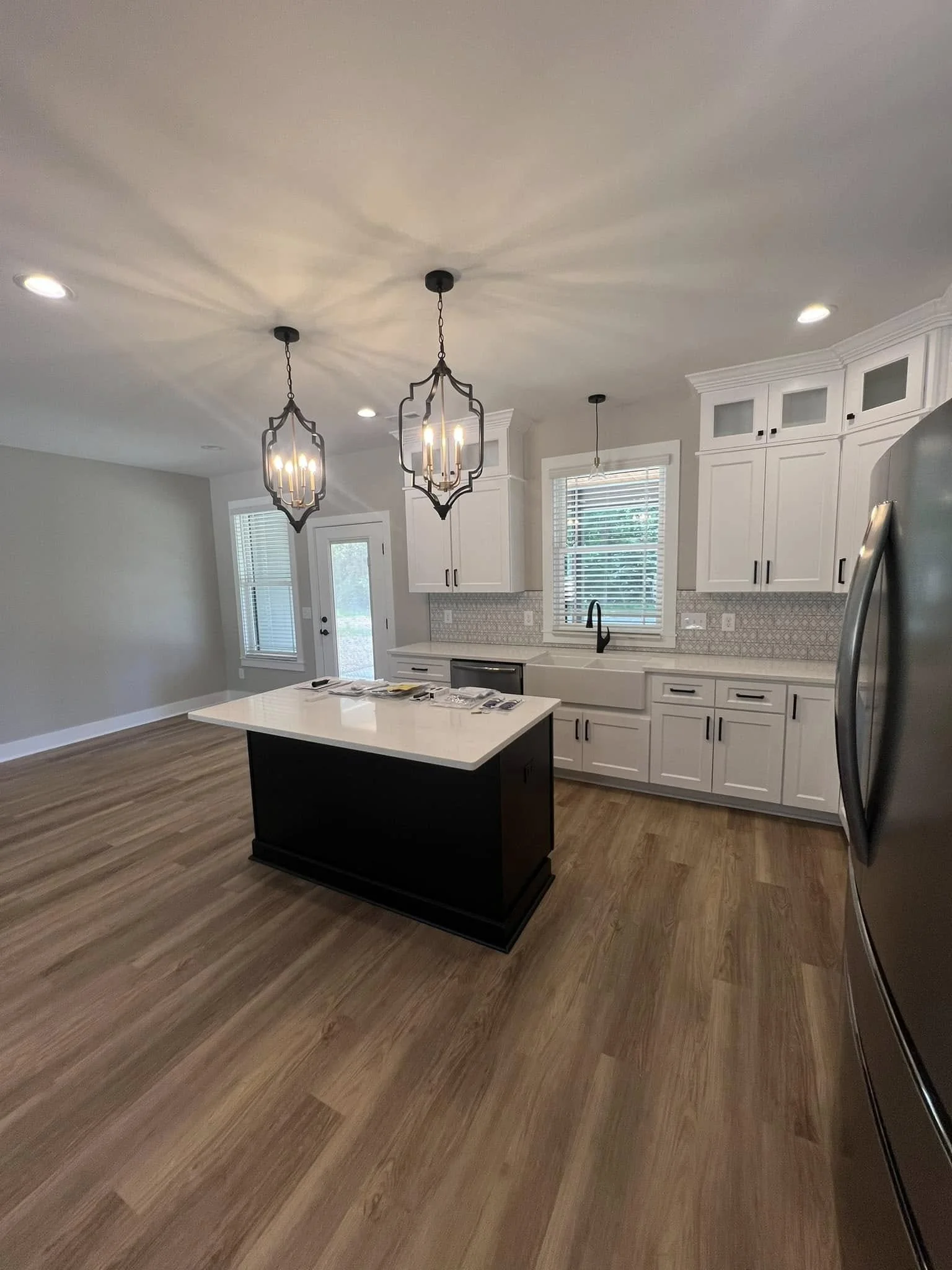 Modern kitchen with white cabinets, a black island with a white countertop, hardwood floors, and two black pendant lights hanging from the ceiling.