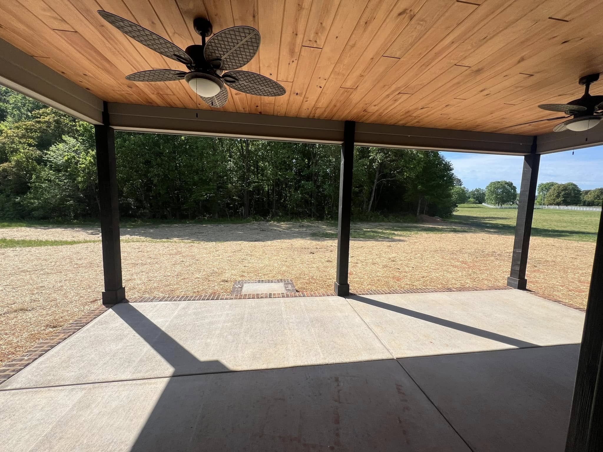 Covered patio with ceiling fans overlooking a grassy yard with trees in the background.